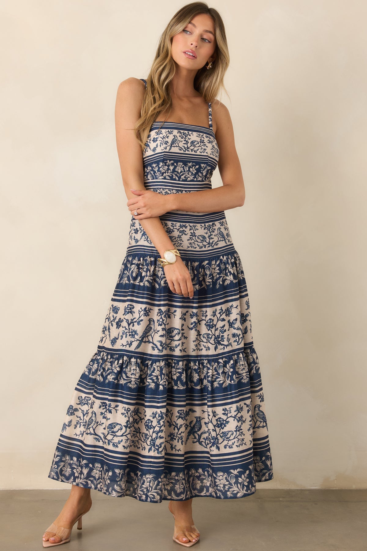 A straight neckline and slender textured straps highlight the fitted bodice above the gathered tiers of the long skirt.