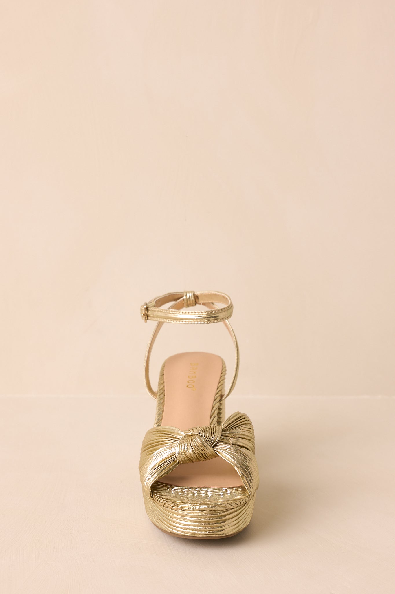 A straight-on shot of the gold heel capturing the open toe design.