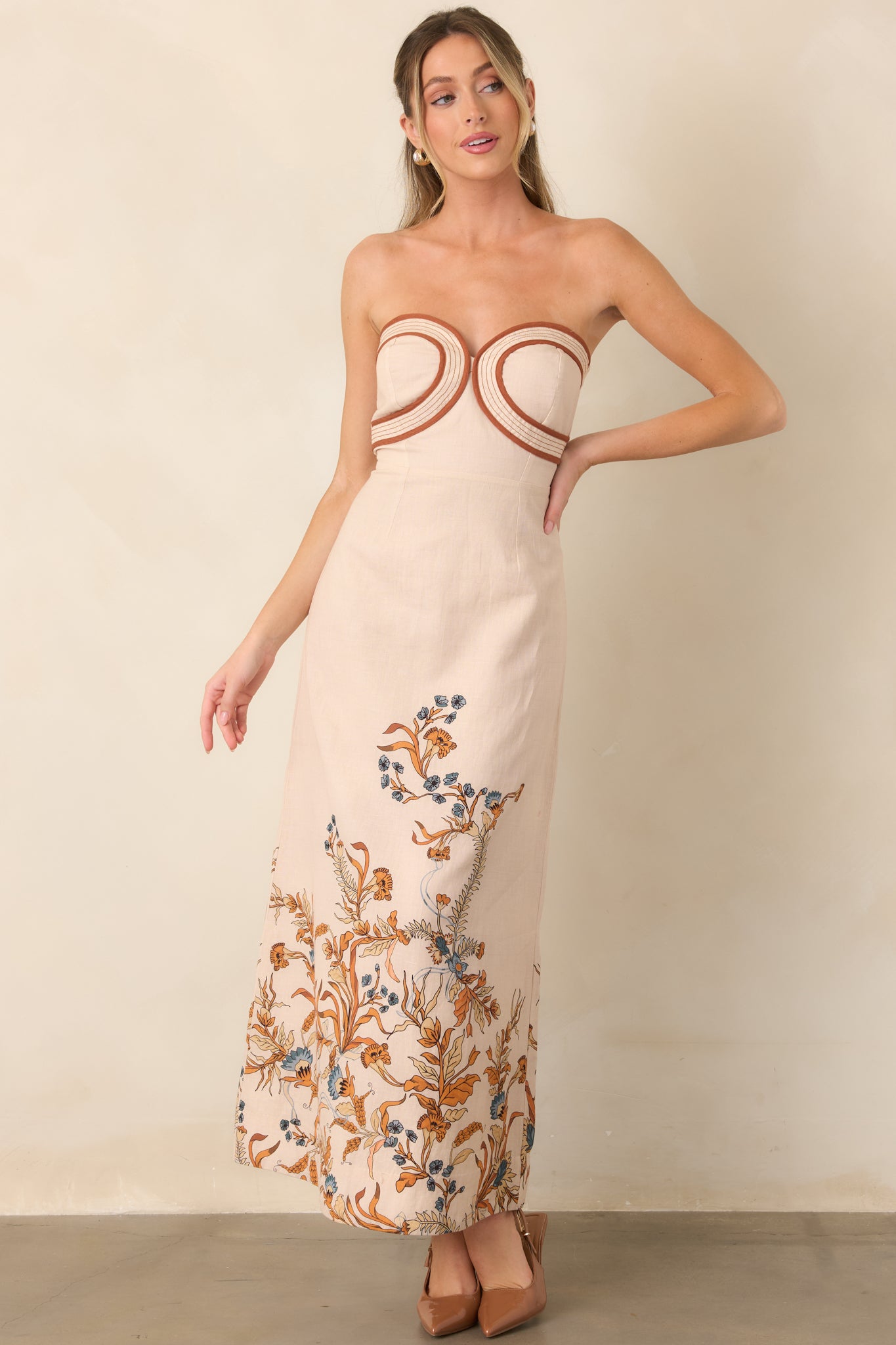 Cotton-linen blend dress with a sculpted strapless bodice, curved contrast trim, fitted waist, and long column-inspired skirt with floral hem detailing.