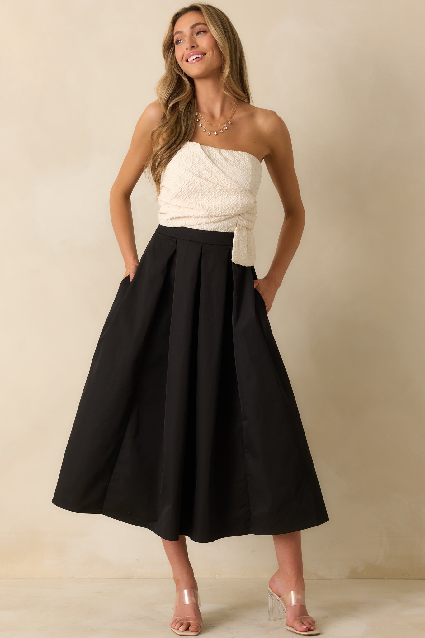 Formal strapless dress featuring a textured ivory bodice, fitted high waist, and full pleated black skirt for an elegant contrast.