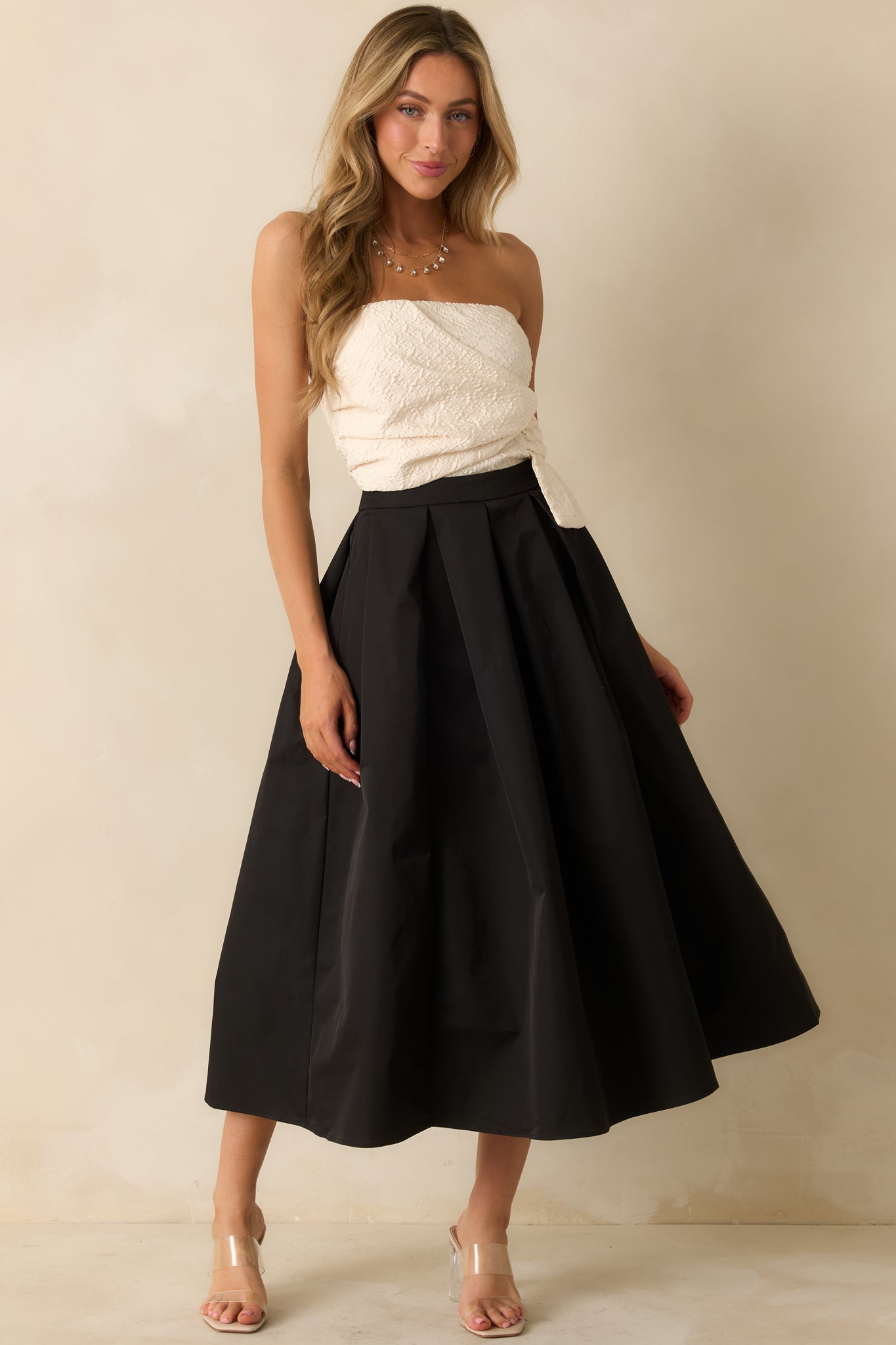 Elegant strapless maxi dress featuring an ivory bodice with wrapped detailing and a voluminous black pleated skirt for a refined silhouette.