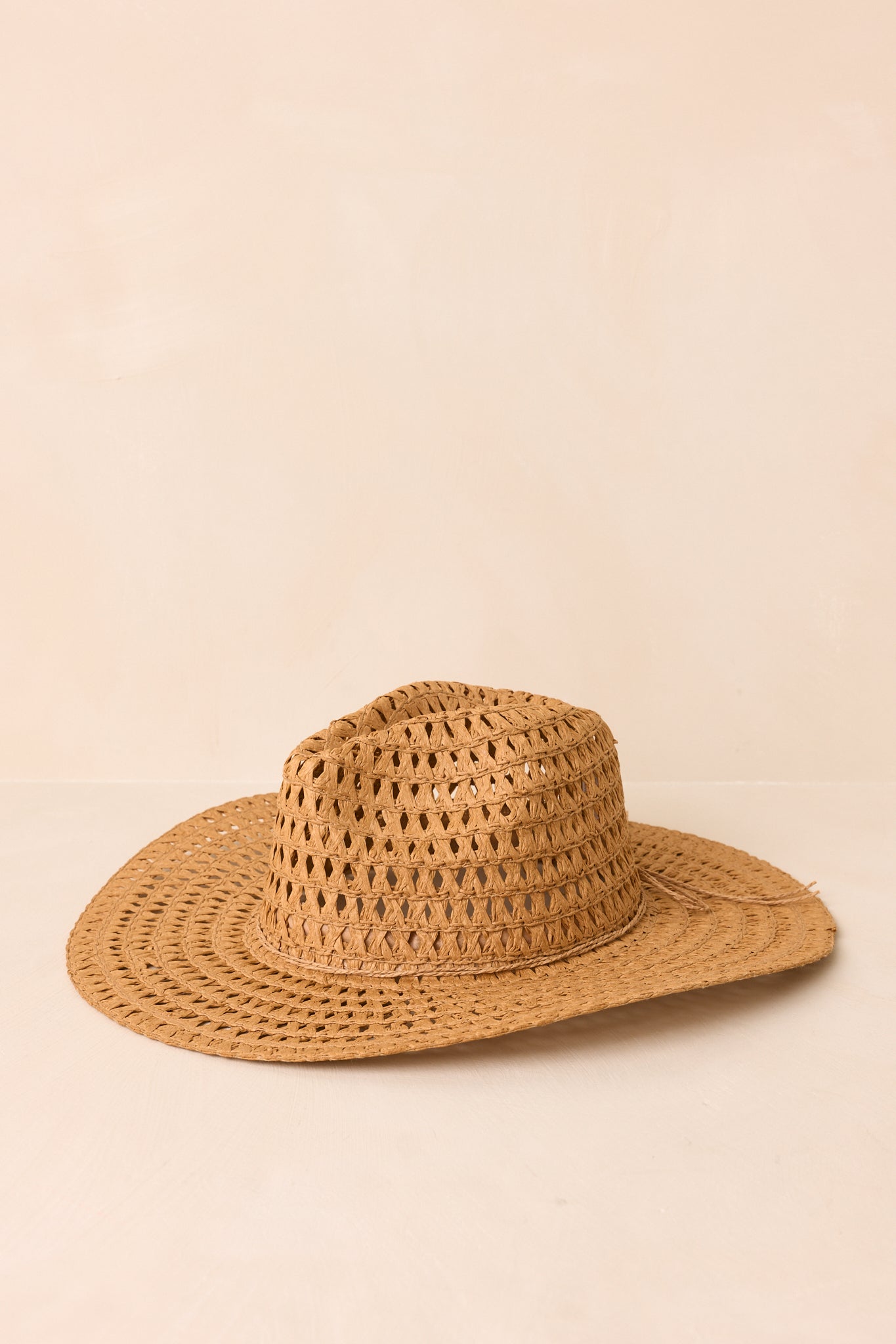 Straw cowboy hat featuring a breathable woven body and timeless wide brim shape displayed on beige.
