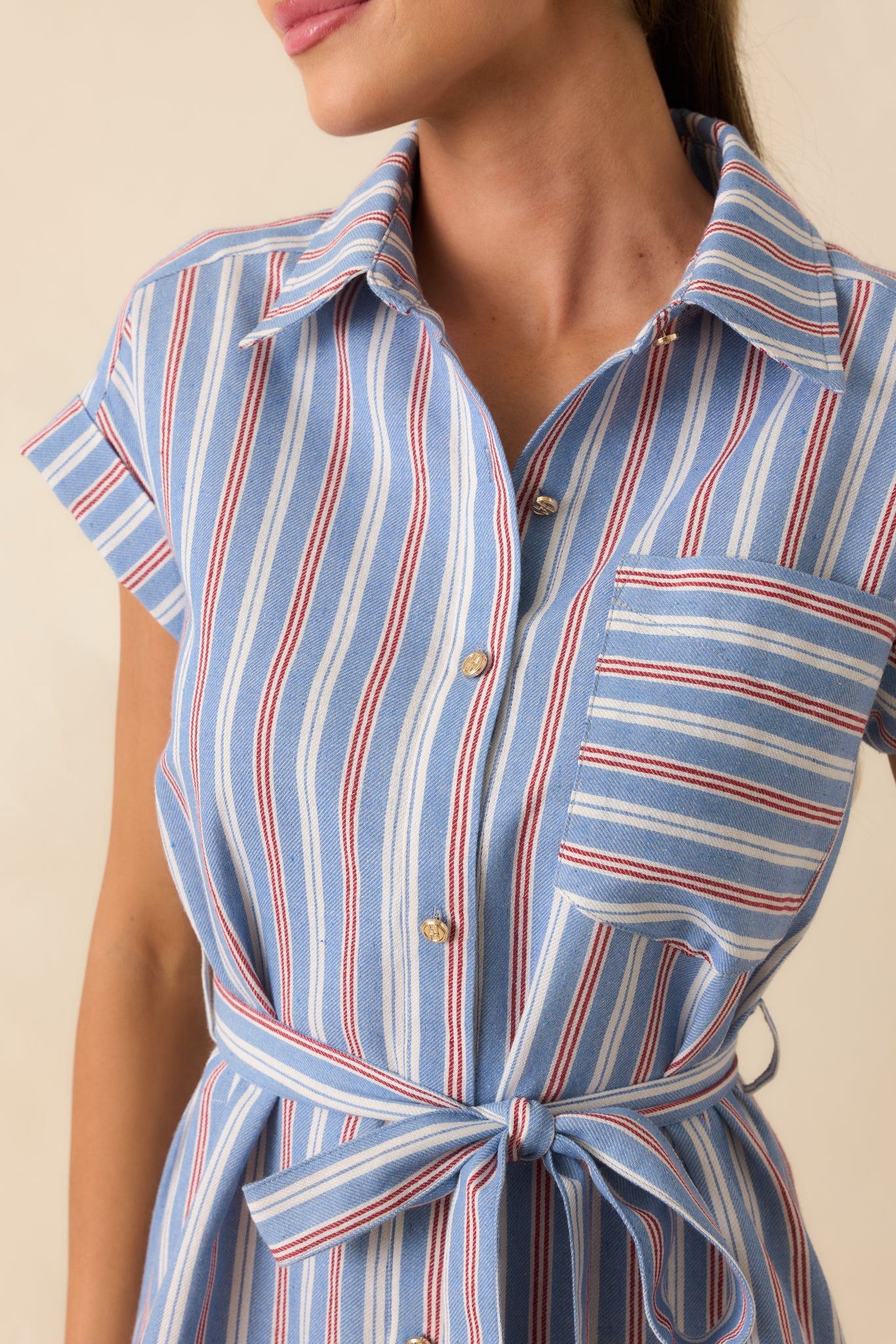 Close-up of the blue, red, and ivory striped fabric highlighting the gold-tone buttons, collared neckline, and chest pocket detail.