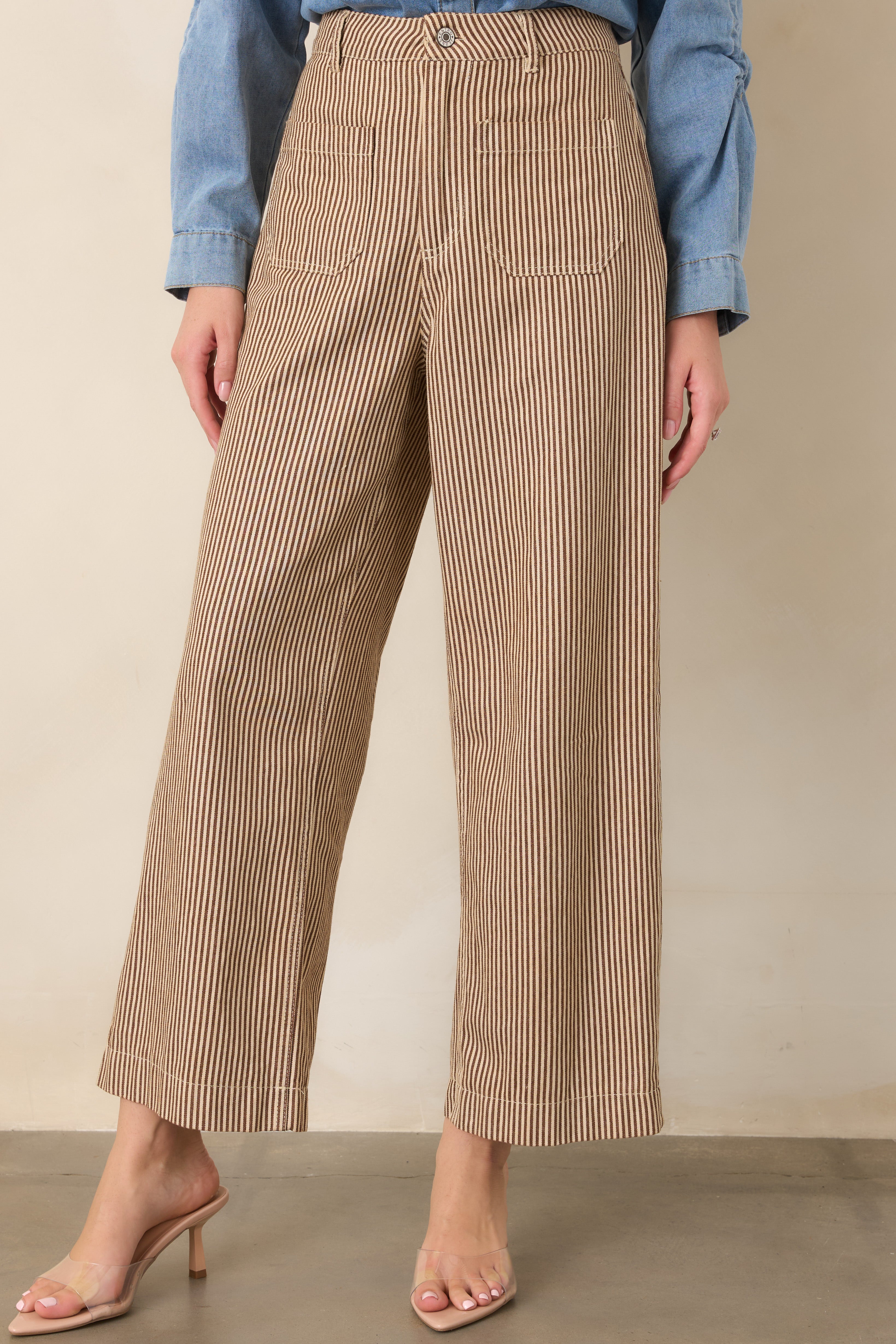 Close view of brown and ivory striped pants showing the high-rise waistband, button and zip closure, and front patch pockets.