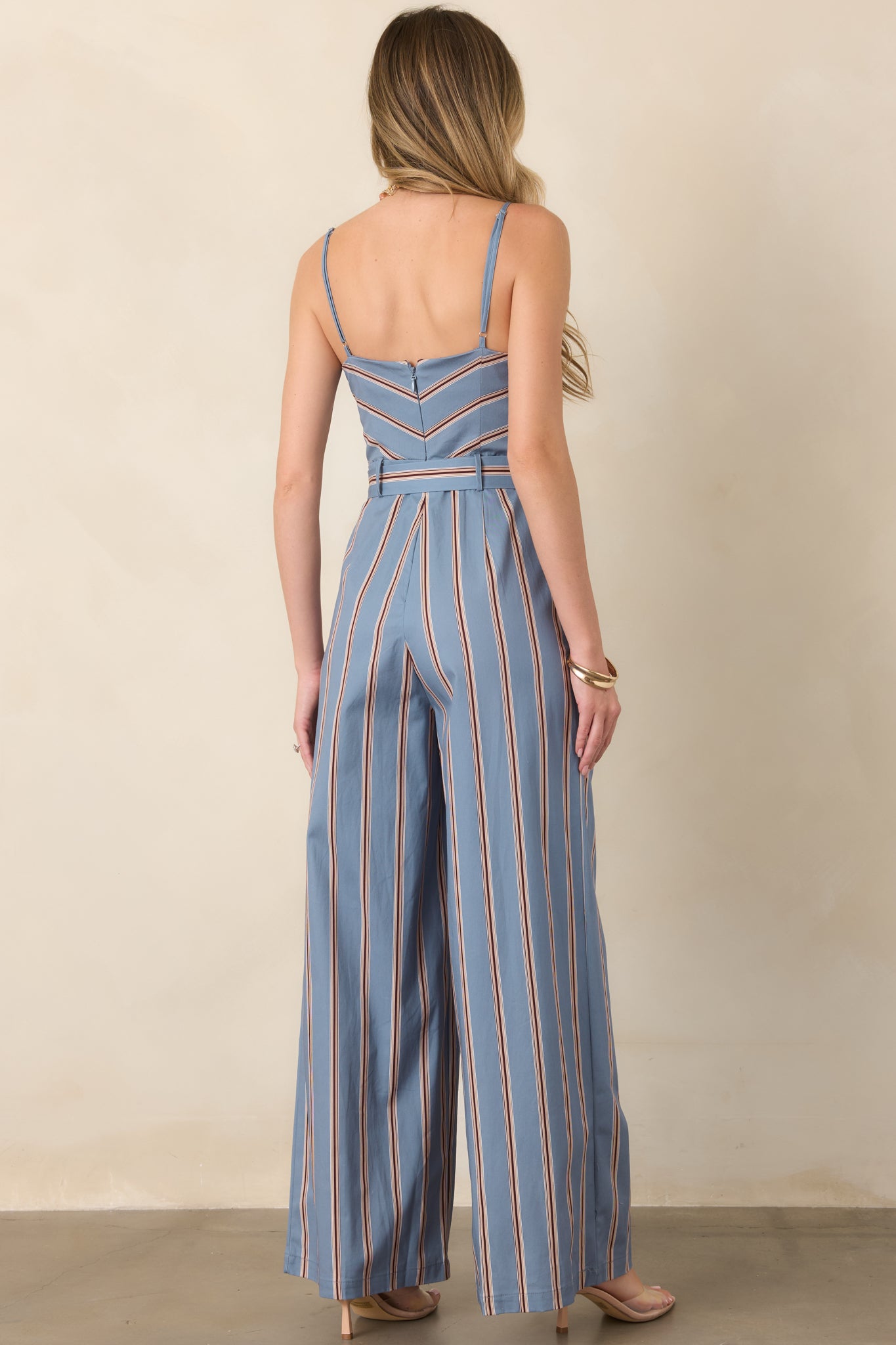 Rear view of the striped jumpsuit showcasing its concealed back zipper, adjustable shoulder straps, matching waist belt, and vertically striped legs.