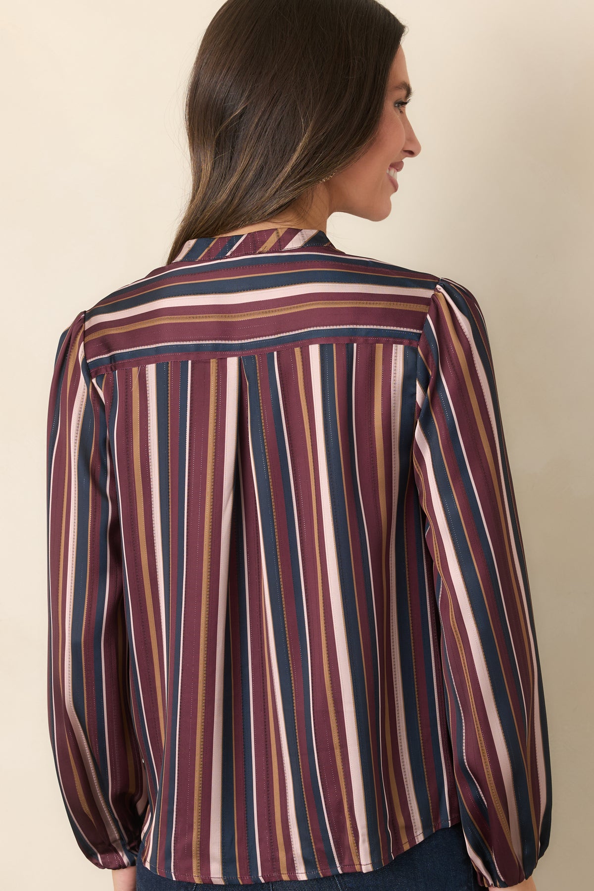 Rear view of the striped satin top showing the back yoke with center pleat, relaxed silhouette, gently curved hem, and long balloon sleeves.