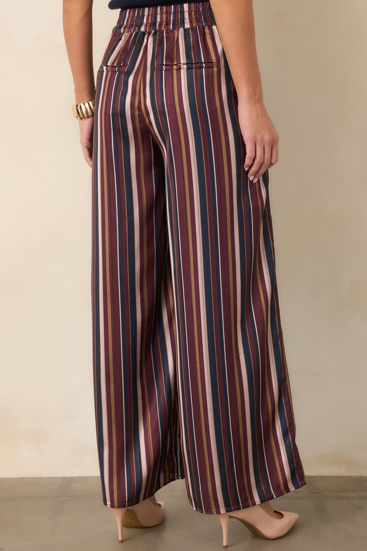 Striped satin pants showcasing the faux welt back pockets and flowing wide leg silhouette from the rear.