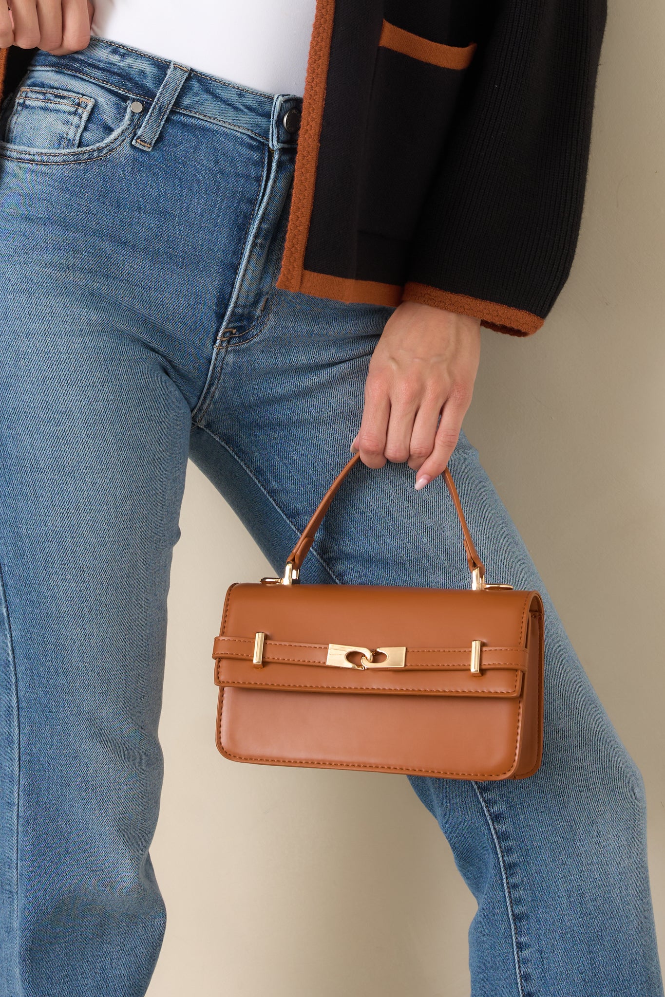 Structured faux leather handbag featuring a polished gold-tone front belt detail, top handle, detachable shoulder strap, and sleek refined silhouette.