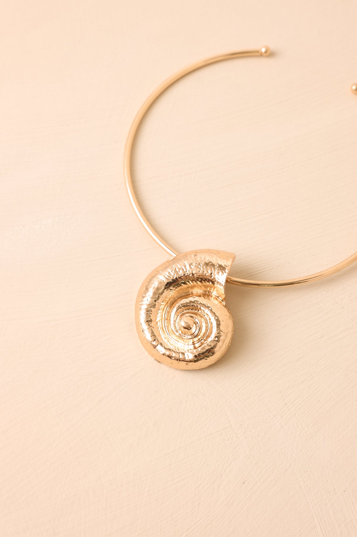 Structured gold-tone necklace on a beige background featuring an open silhouette and bold spiral detailing.