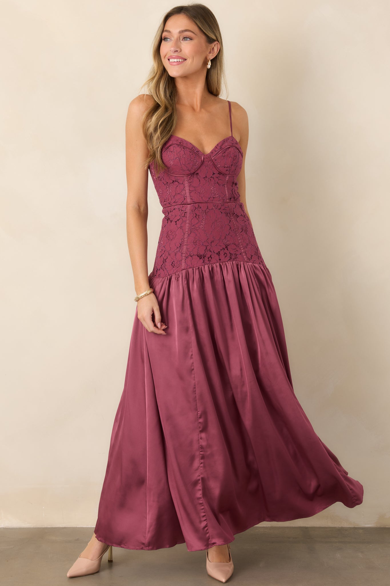 Elegant maxi dress showcasing its structured lace bodice, sweetheart neckline, slender straps, elongated dropped-waist silhouette, and fluid satin skirt.