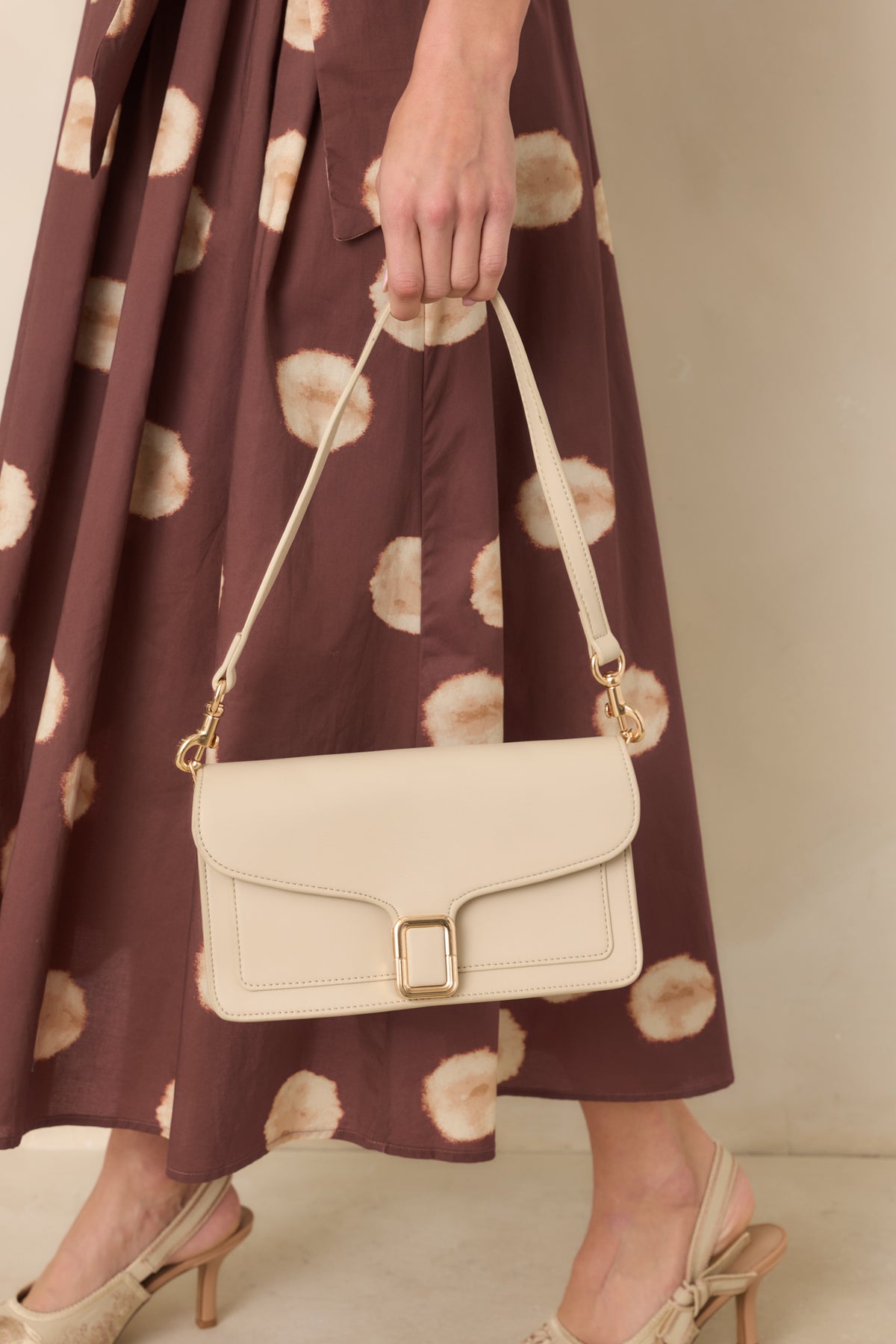 Structured off-white handbag featuring smooth faux leather, tonal edge stitching, a polished gold-tone buckle, and detachable shoulder strap.