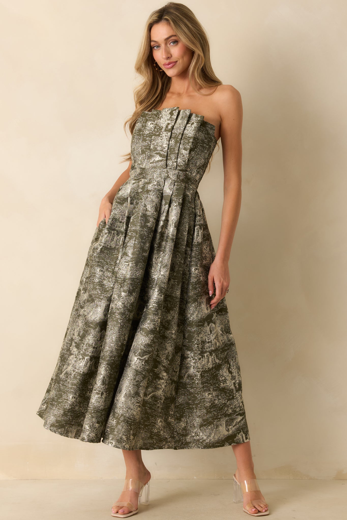 Structured strapless olive dress featuring a fitted pleated bodice, flowing A-line skirt, and detailed ivory jacquard design.