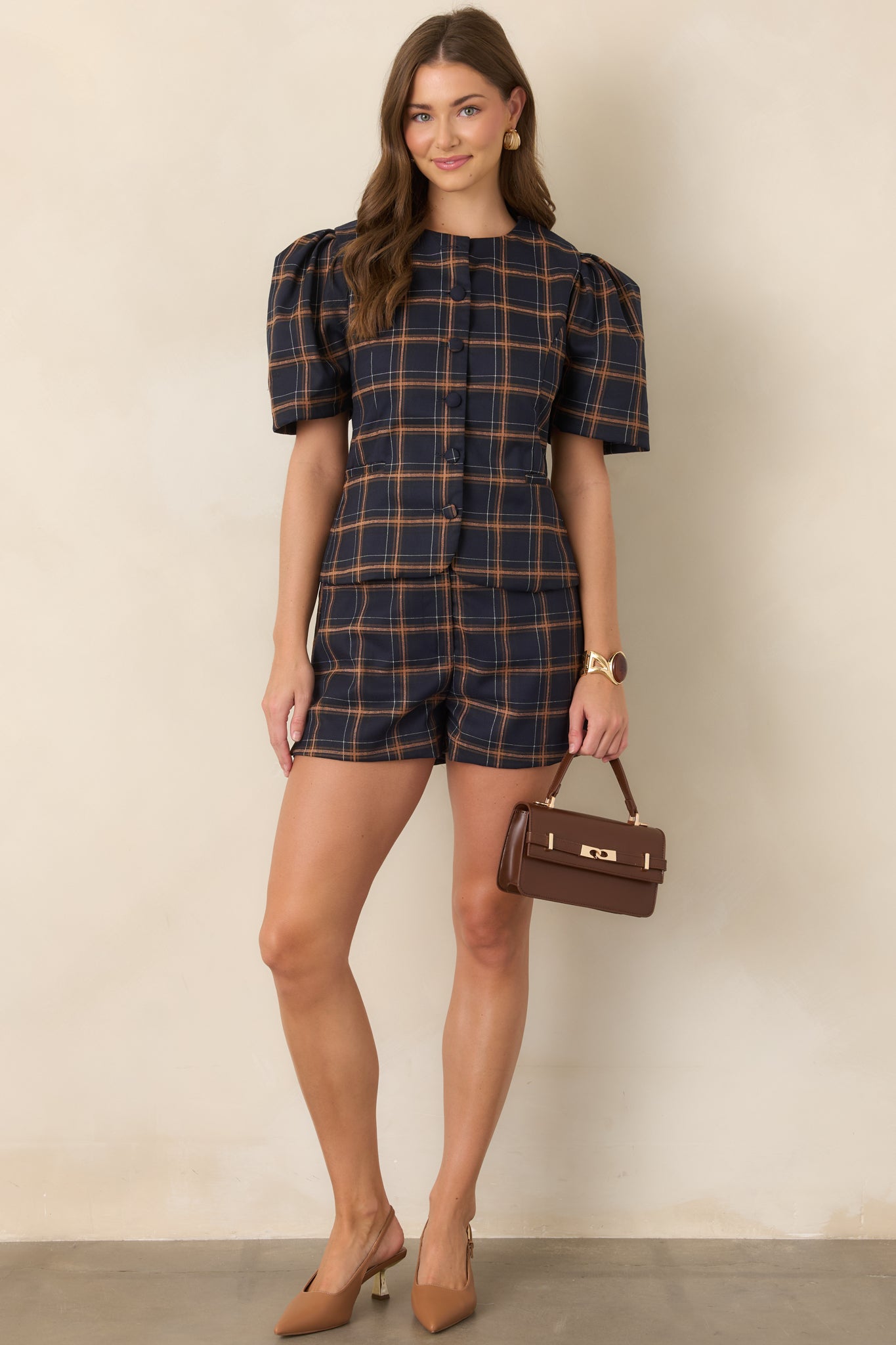 Structured woven plaid top in navy with camel and ivory accents, designed with dramatic puff sleeves, a button-front closure, and tailored seams that create a defined waist.