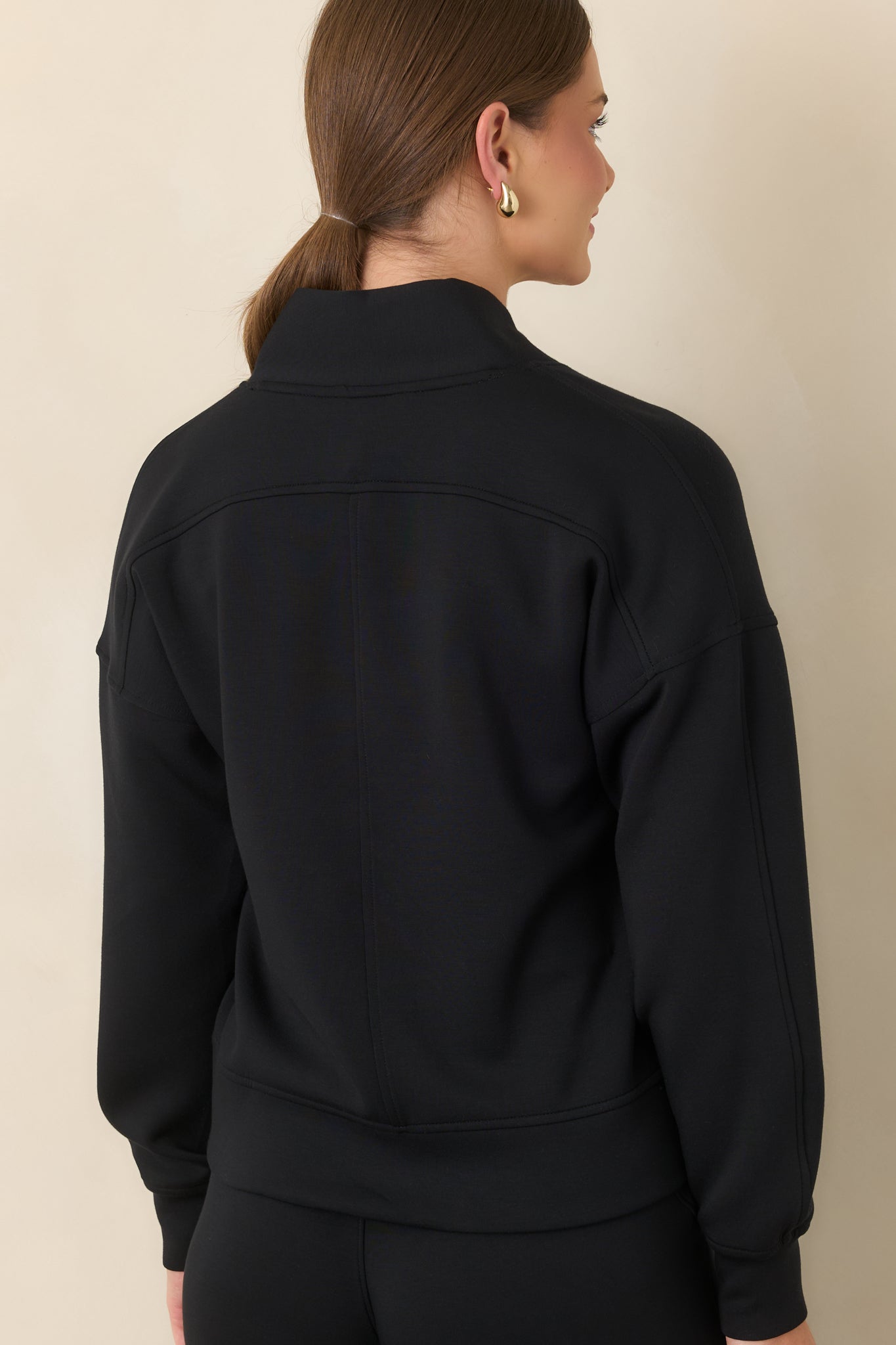 Rear view of the structured top showing its dropped shoulders, long sleeves, and banded cuffs.