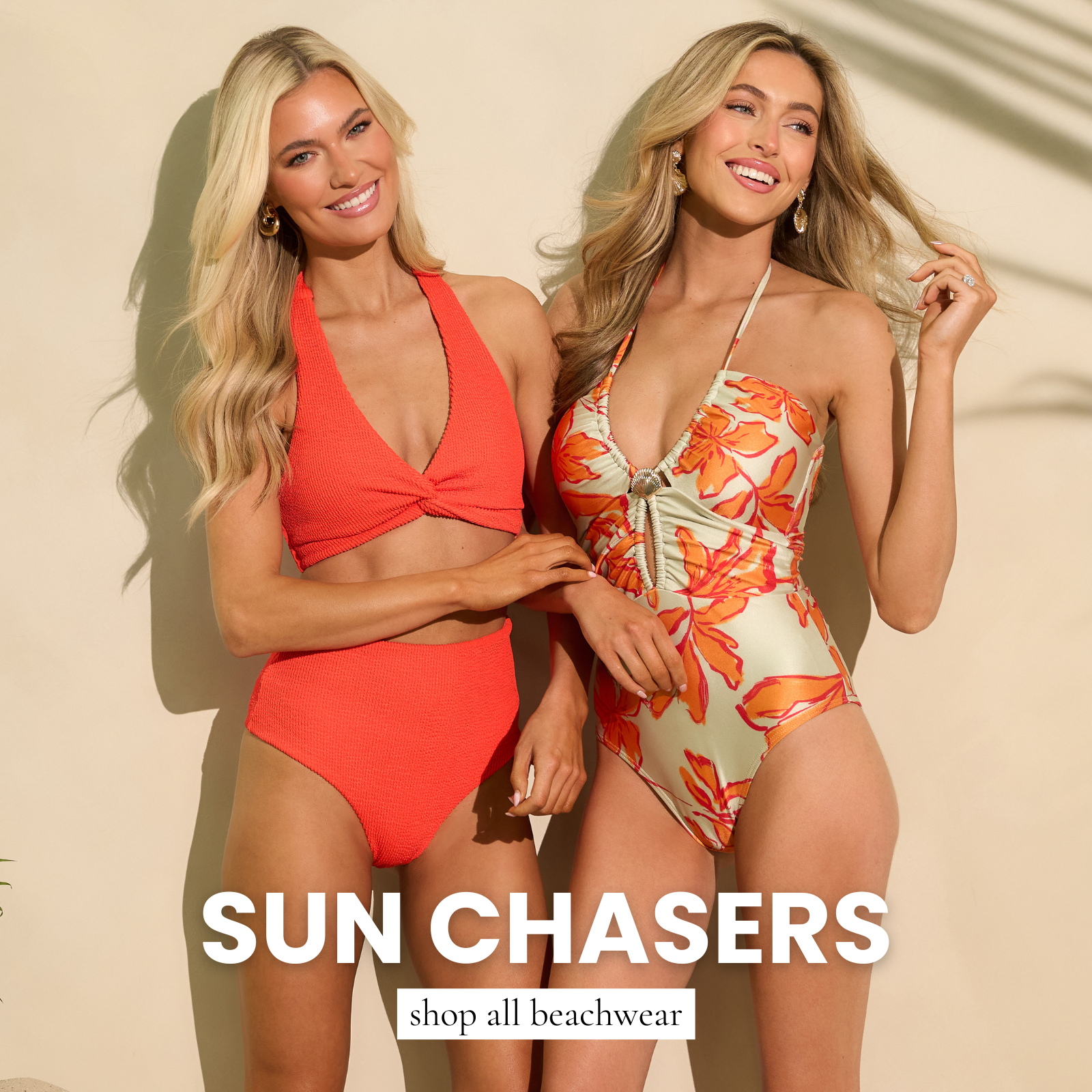 Two models smiling in bright beachwear against a sunny neutral backdrop. One wears an orange textured bikini set, and the other wears a floral halter one-piece swimsuit. Both pieces are featured in our Beachwear Shop.