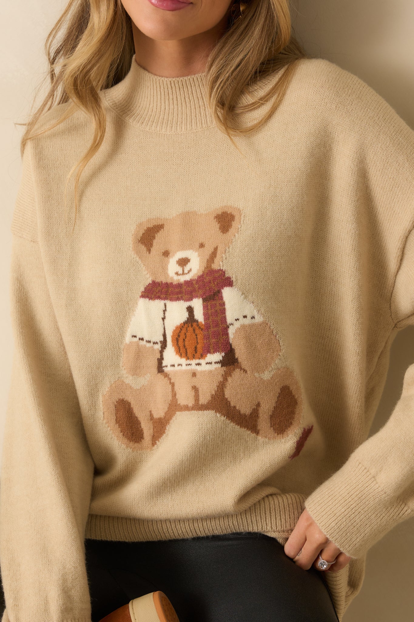A close-up of the sweater fabric showing intarsia knit teddy bear, knit texture, and ribbed trim details.