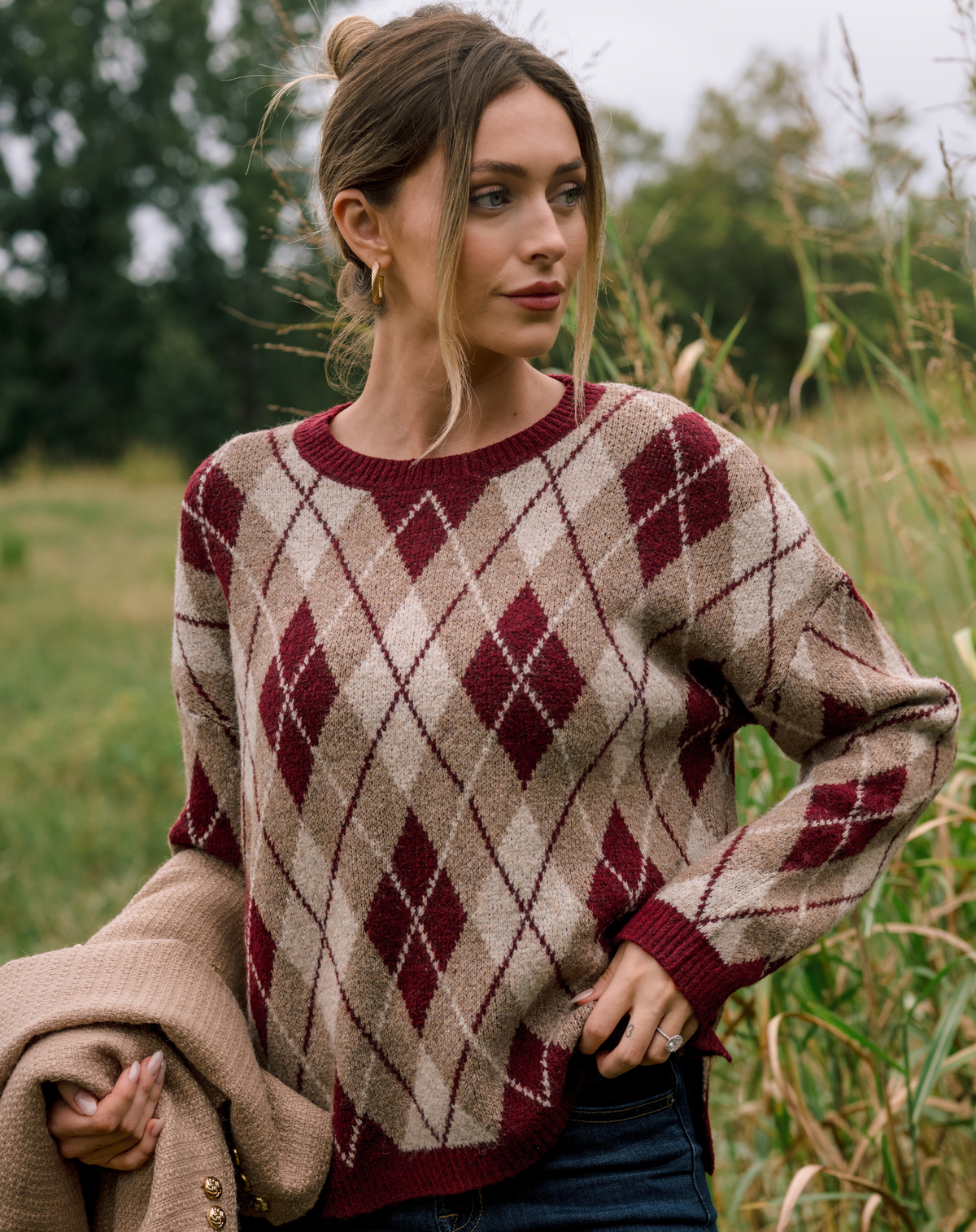 Model wearing a red and tan argyle sweater with jeans.