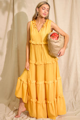 Full front view of this sunset yellow dress that features a ruffled v-neckline with a self-tie closure, a sleeveless design, and a flowy skirt with subtle ruffle detailing throughout.