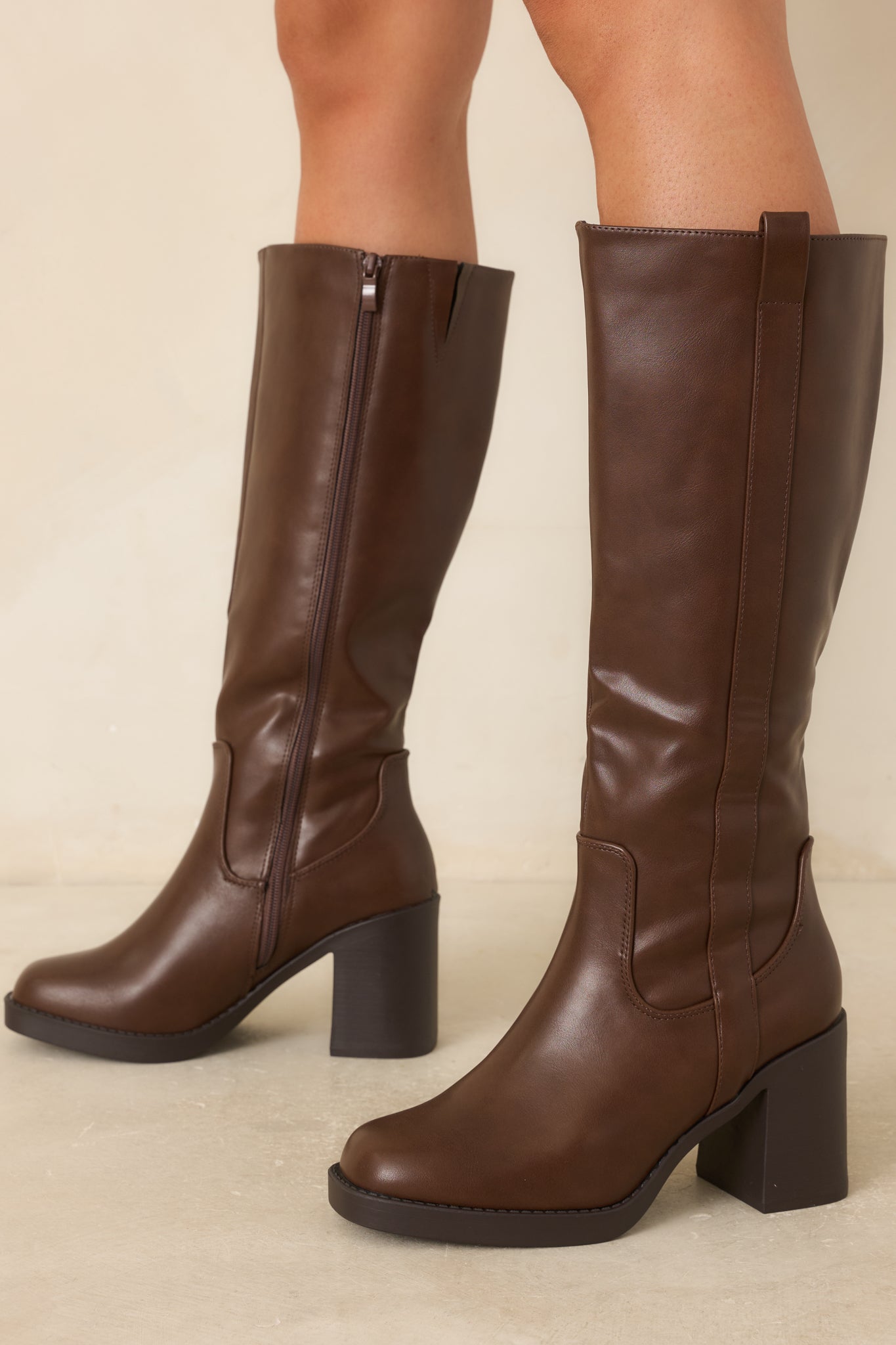 Smooth faux leather tall boots showcasing curved paneling, welt-style stitching, a full-length side zipper, and a modern block heel design.
