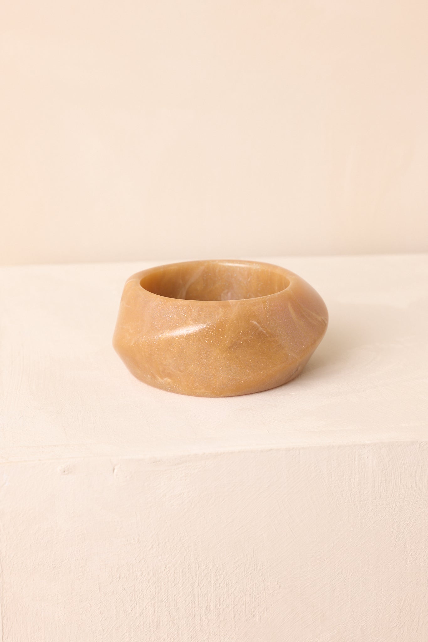 The tan acrylic bangle on a beige background, emphasizing its chunky width and shimmering glitter accents.