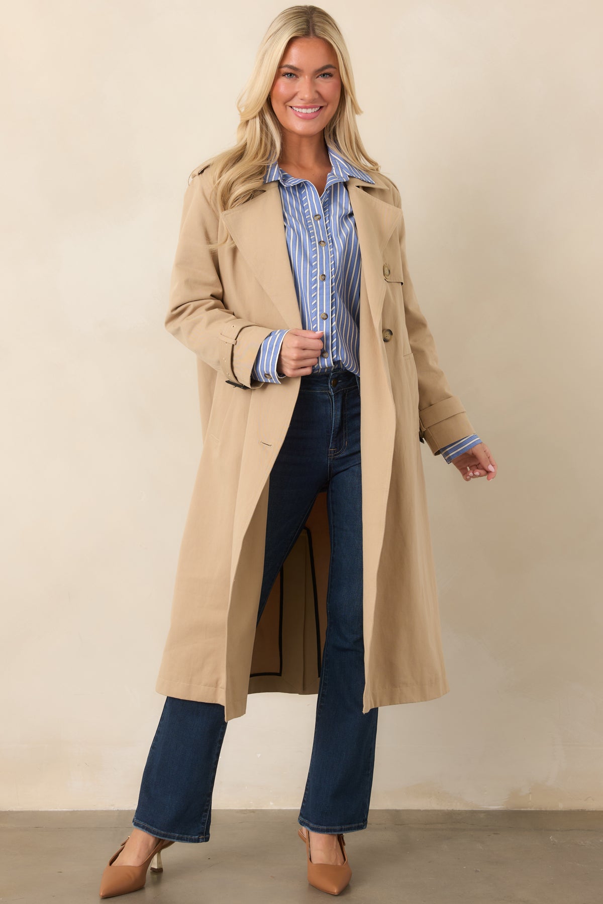 Tan trench coat showcasing its belted waist, wide notched lapels, double-breasted front, and softly structured full-length silhouette.