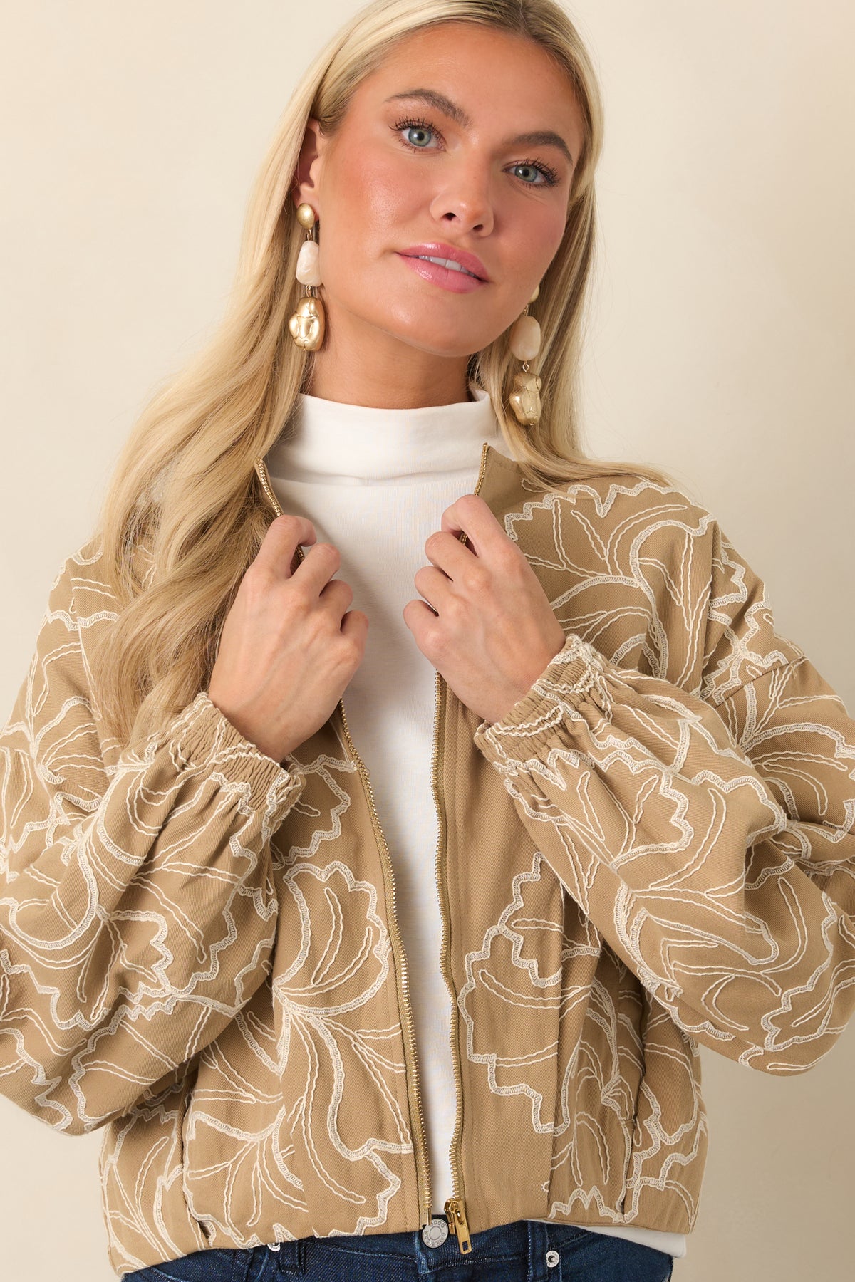 Tan cotton jacket showcasing the textured floral embroidery and refined gold-tone zipper hardware.