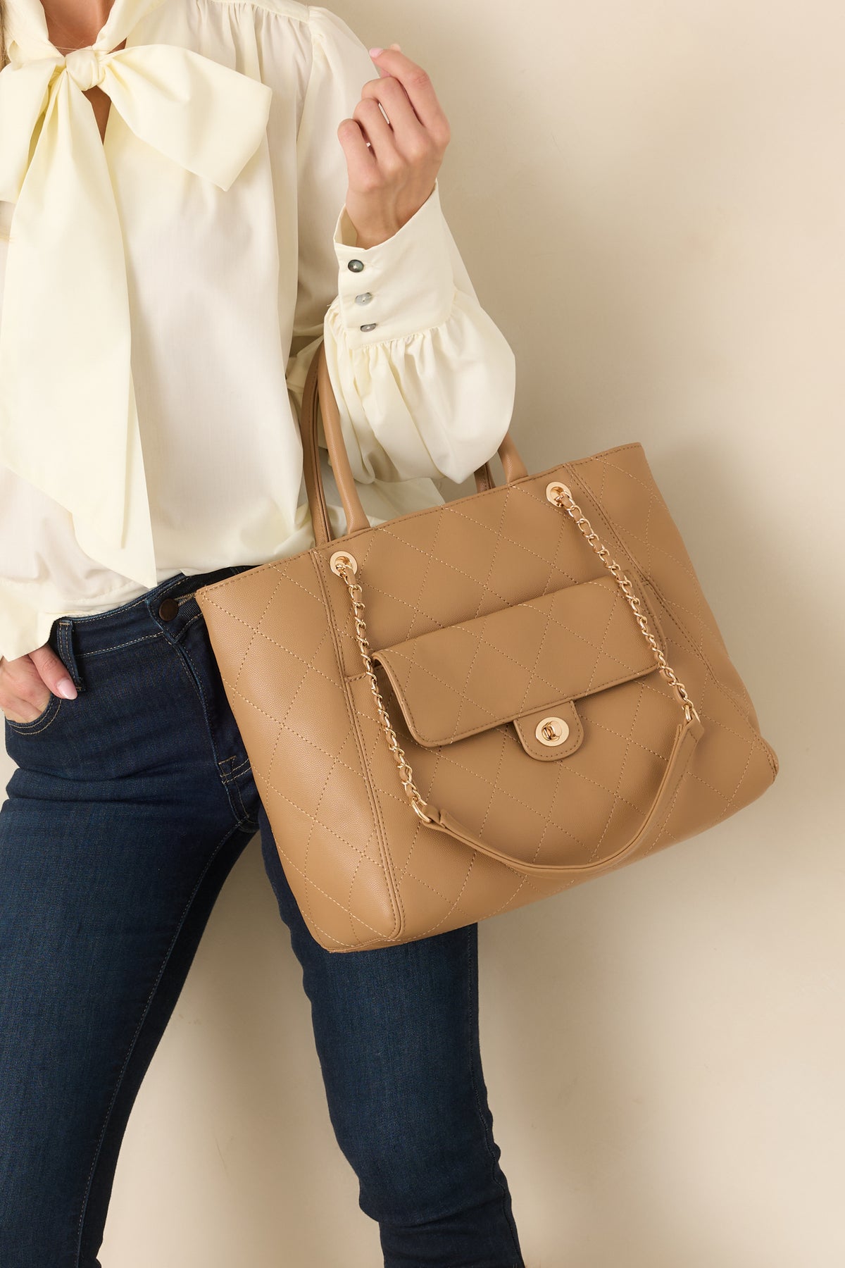 Tan diamond-quilted handbag features gold-tone hardware, top handles, chain-accented shoulder straps, and a front twist-lock pocket.