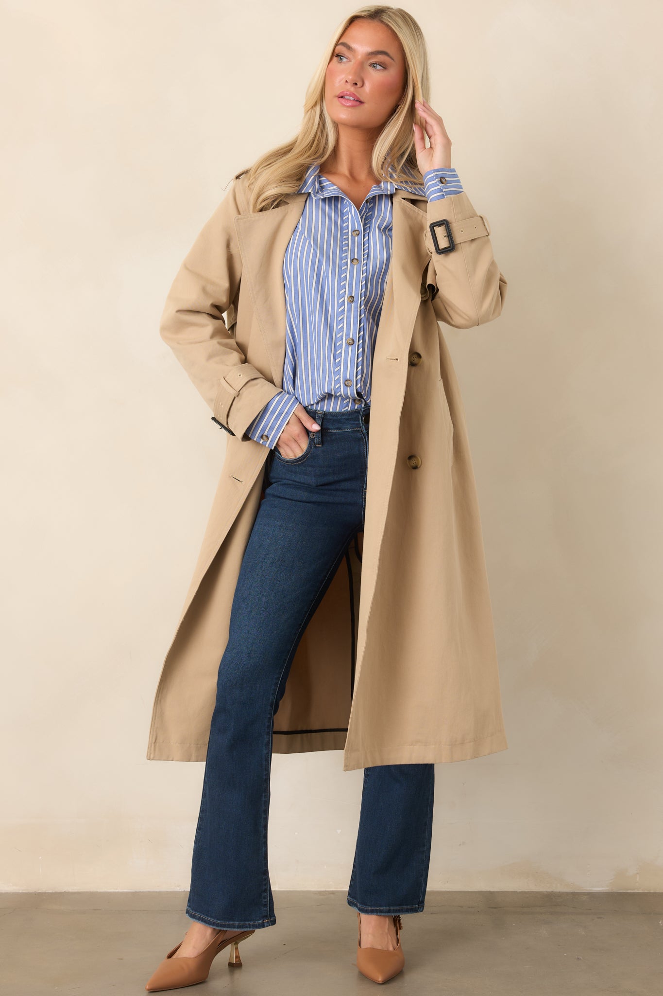 Tan trench coat featuring a double-breasted front, notched lapels, removable tie belt, side pockets, and a long polished silhouette.