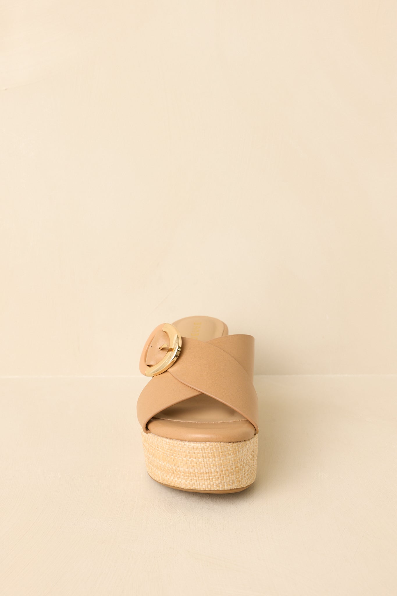Close cropped angle of tan platform wedges highlighting the natural-toned wedge base and bold buckle accent.