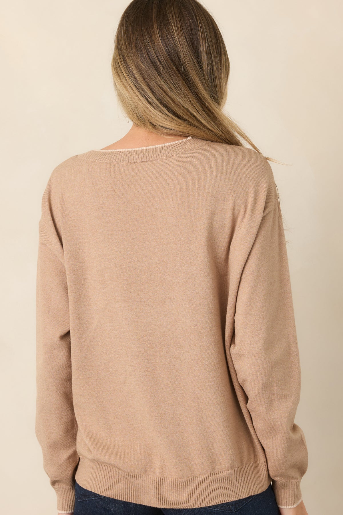 Rear view of the tan top showing its relaxed silhouette, long sleeves, and ribbed hem and cuffs.