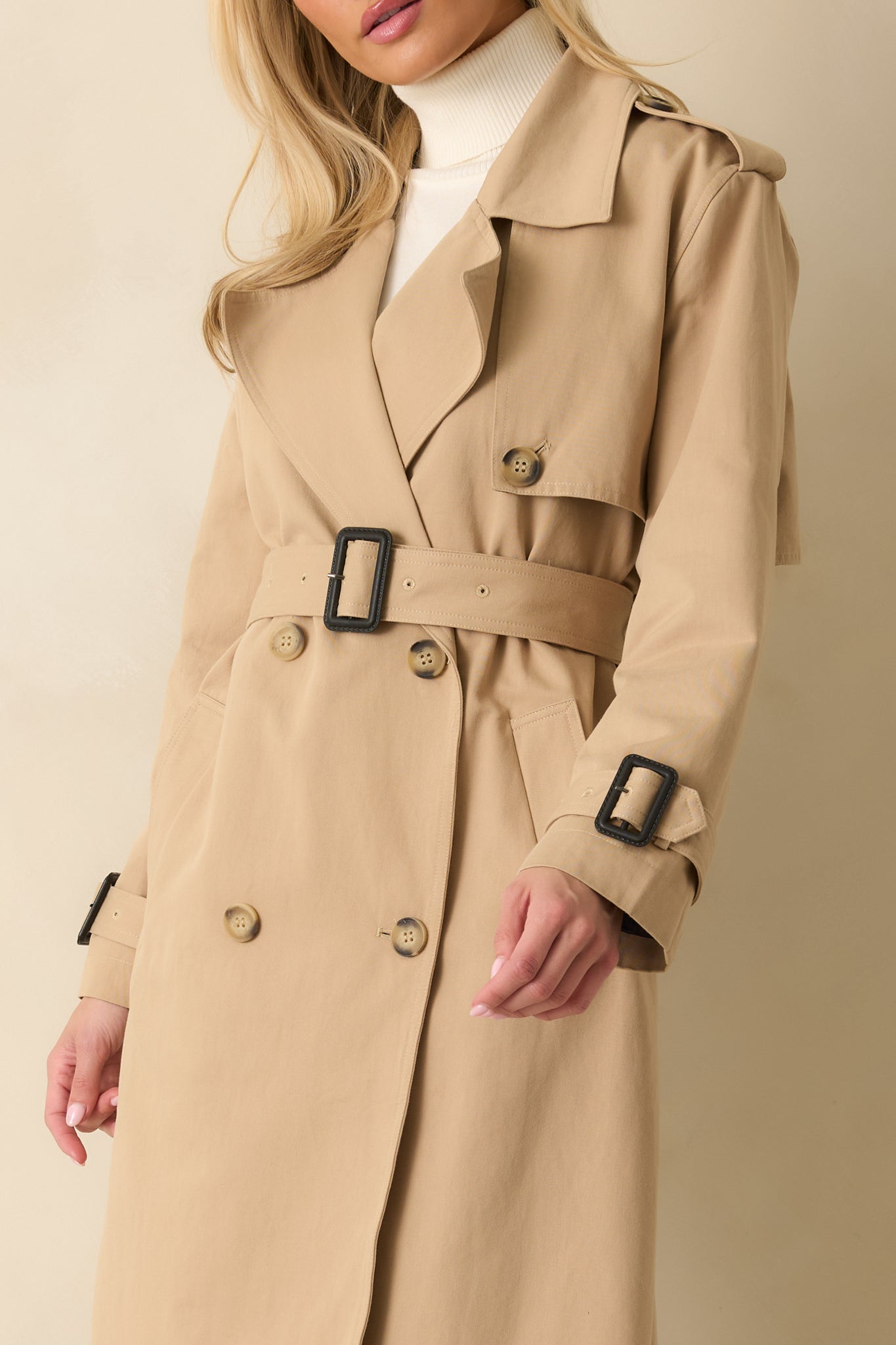 Detailed look at the fabric texture, button closures, and belt of the tan trench coat.