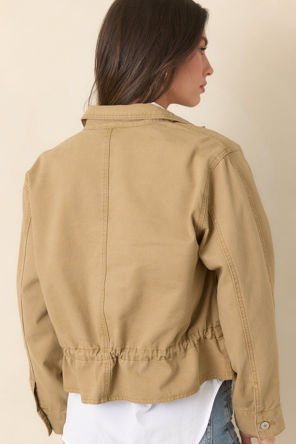 Rear of the tan utility jacket showcases its relaxed shape, long sleeves, and adjustable drawcord hem.