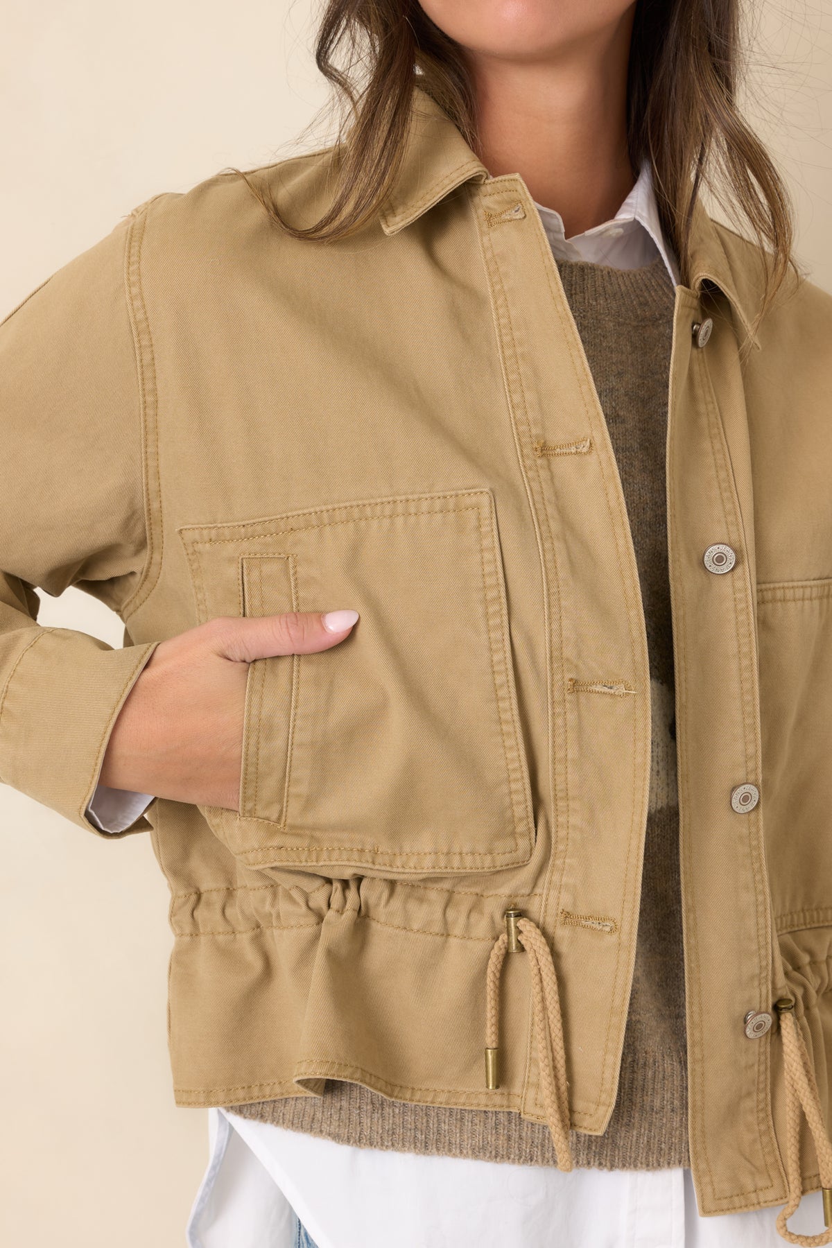 Close-up highlights the woven tan fabric, front buttons, and stitching around the utility jacket's patch pockets.