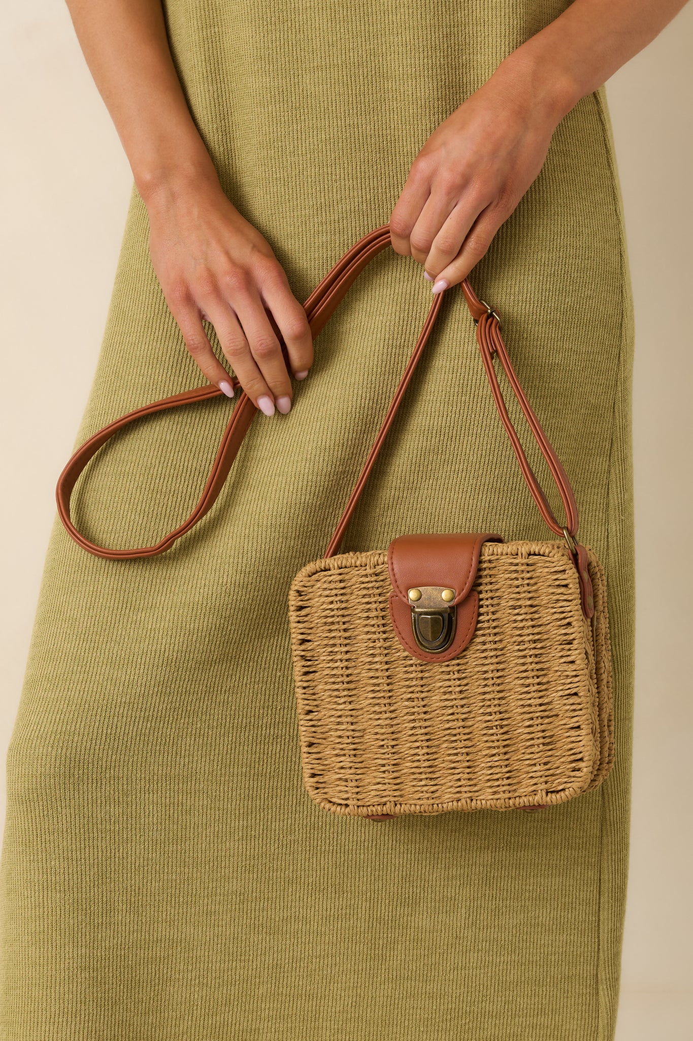 Tan wicker handbag highlighting the textured woven material, bronze hardware, and brown faux leather strap.