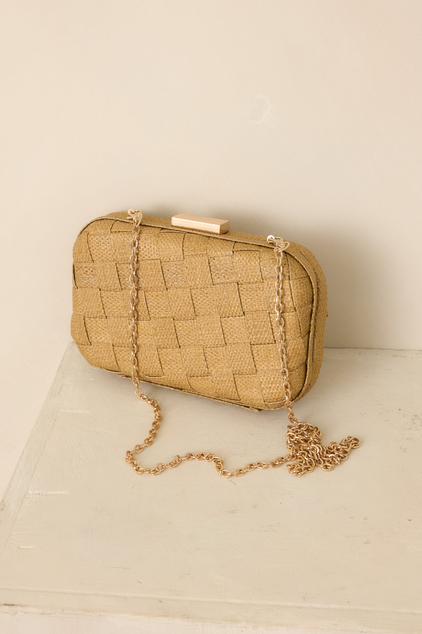 Textured woven clutch in tan with a compact silhouette and removable gold-tone chain for hands-free carrying.
