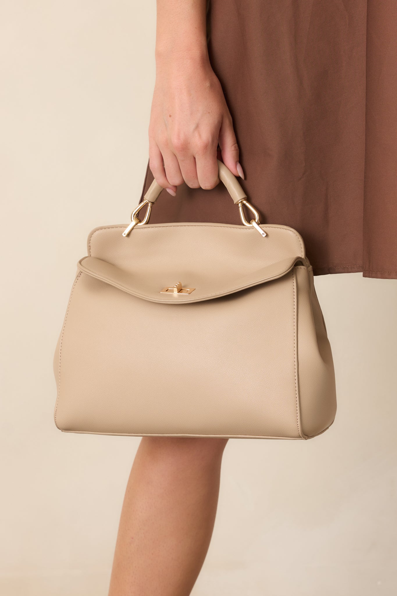 Close-up of the taupe faux leather handbag’s gold-tone twist lock closure and top handle.