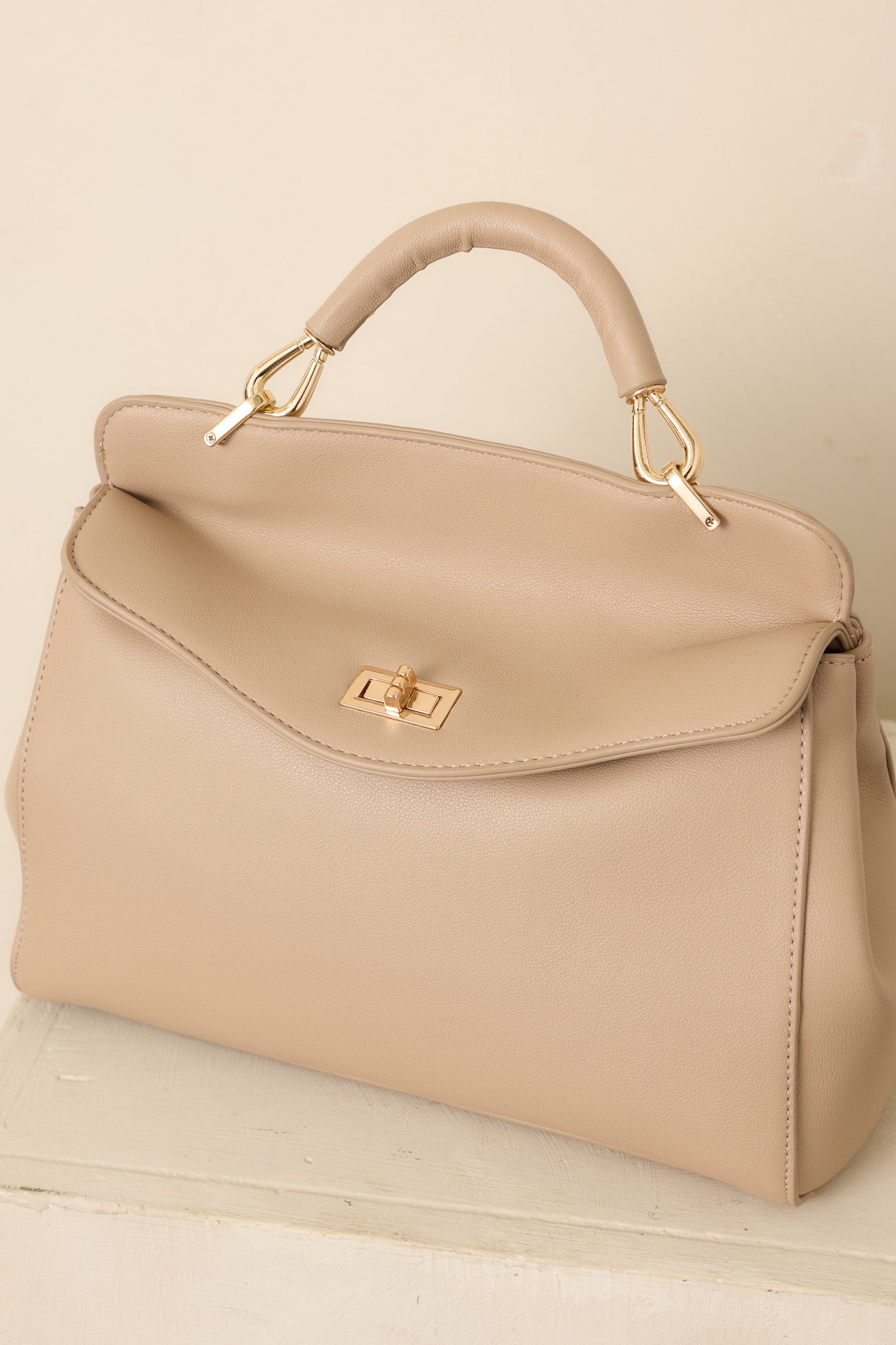 Taupe faux leather handbag showcasing its structured shape, top handle, and elegant gold-tone twist lock closure.