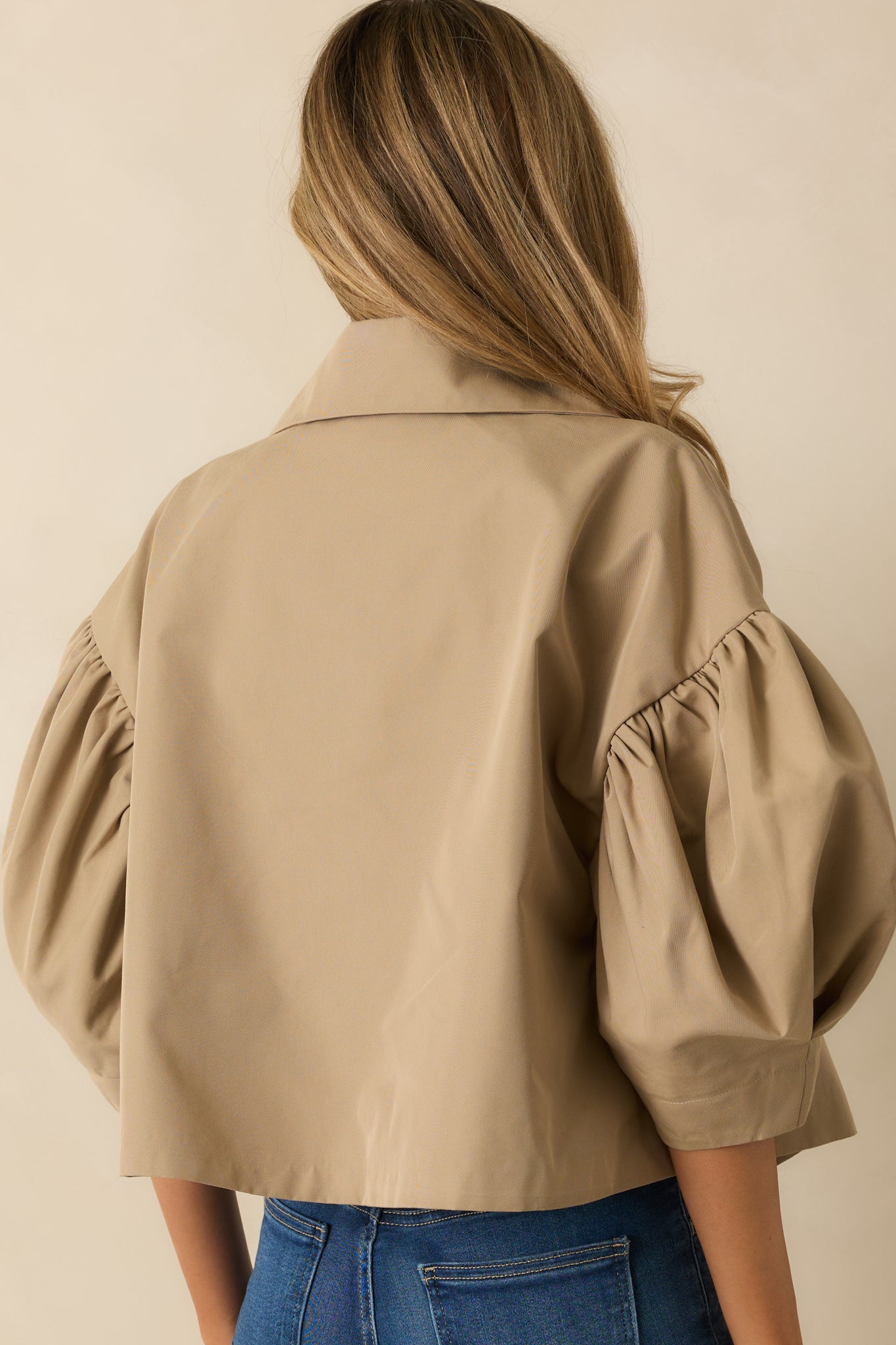 Rear view of taupe jacket showing puff sleeves, cropped hem, and smooth woven finish.