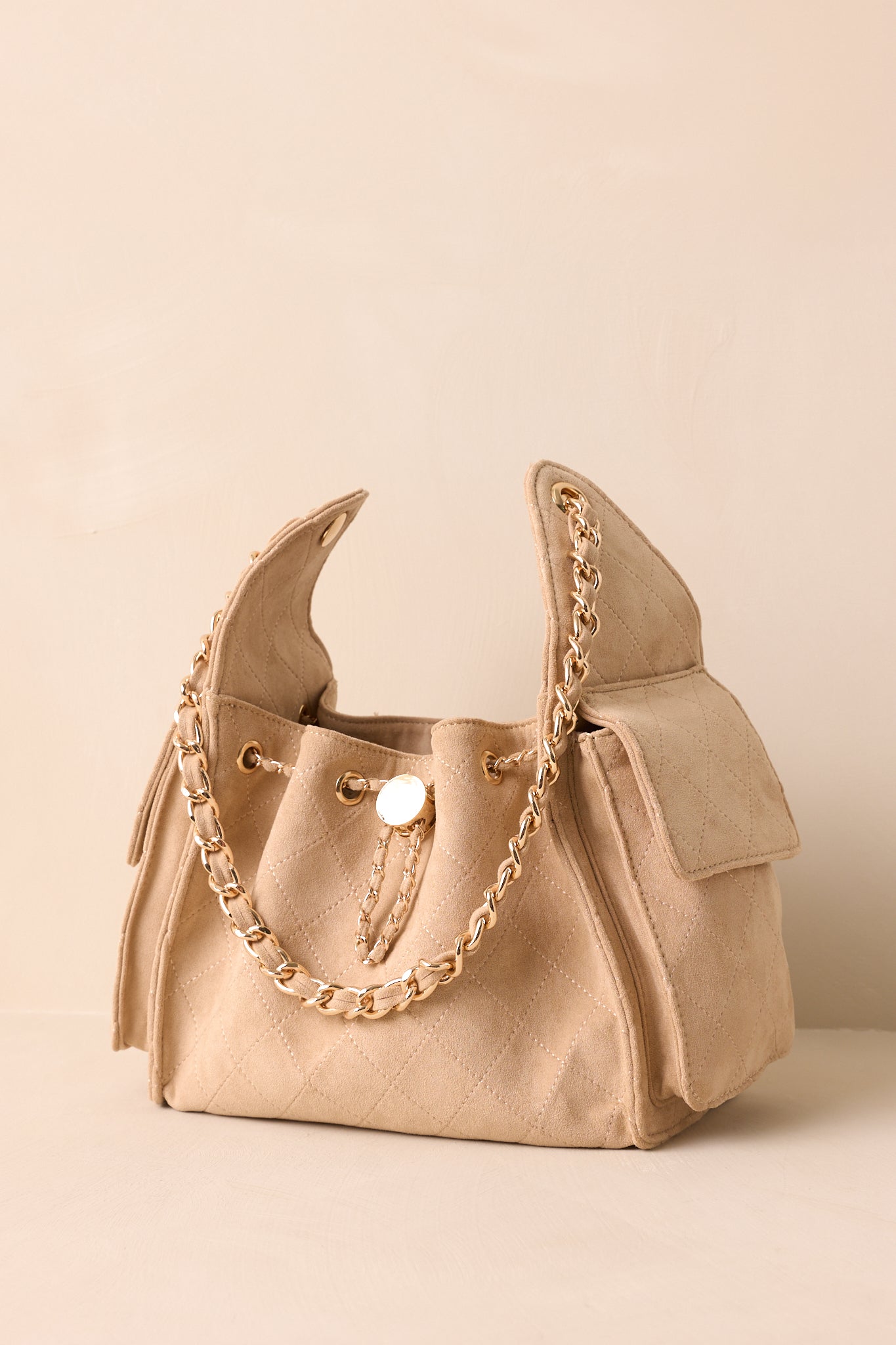 Taupe quilted faux leather purse with gold drawstring closure, fold-over side pockets, and detachable strap, shown from the front.