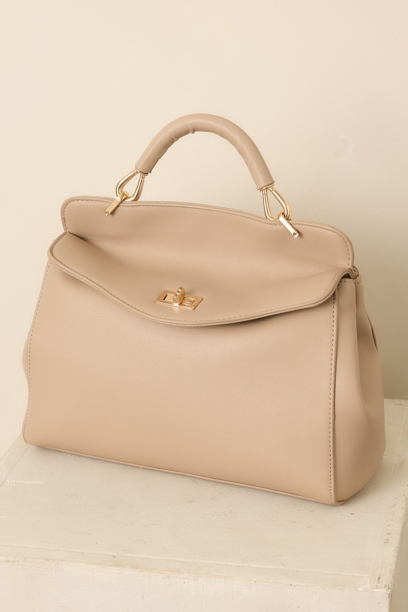 Taupe faux leather handbag with a structured silhouette, top handle, gold-tone twist lock closure, and optional shoulder strap.