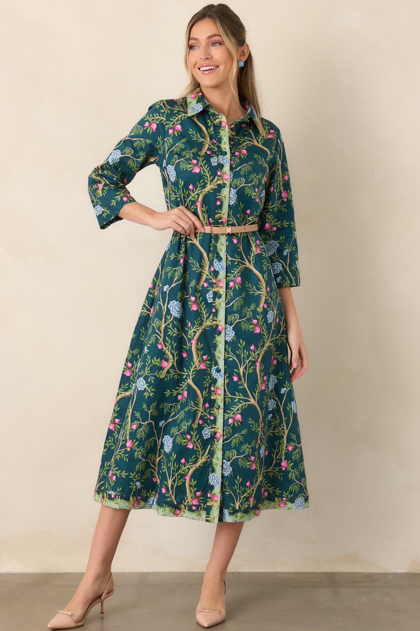 Deep teal cotton midi dress featuring a botanical print of tan branches, green leaves, pink buds, and soft blue flowers, with a collared neckline, three-quarter sleeves, and full button front.