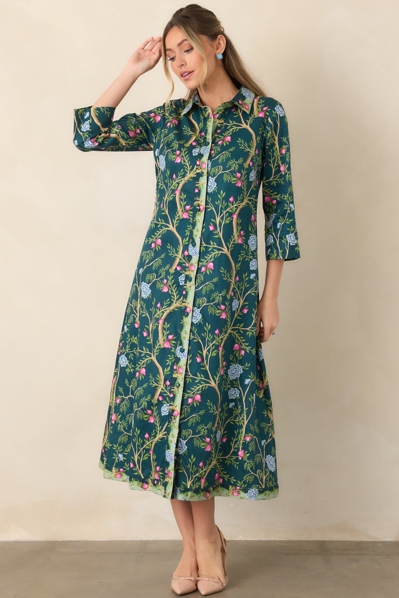 Colorful cotton dress featuring a deep teal ground, tan branch motif, multicolor floral accents, contrasting green placket, and tailored collared silhouette.
