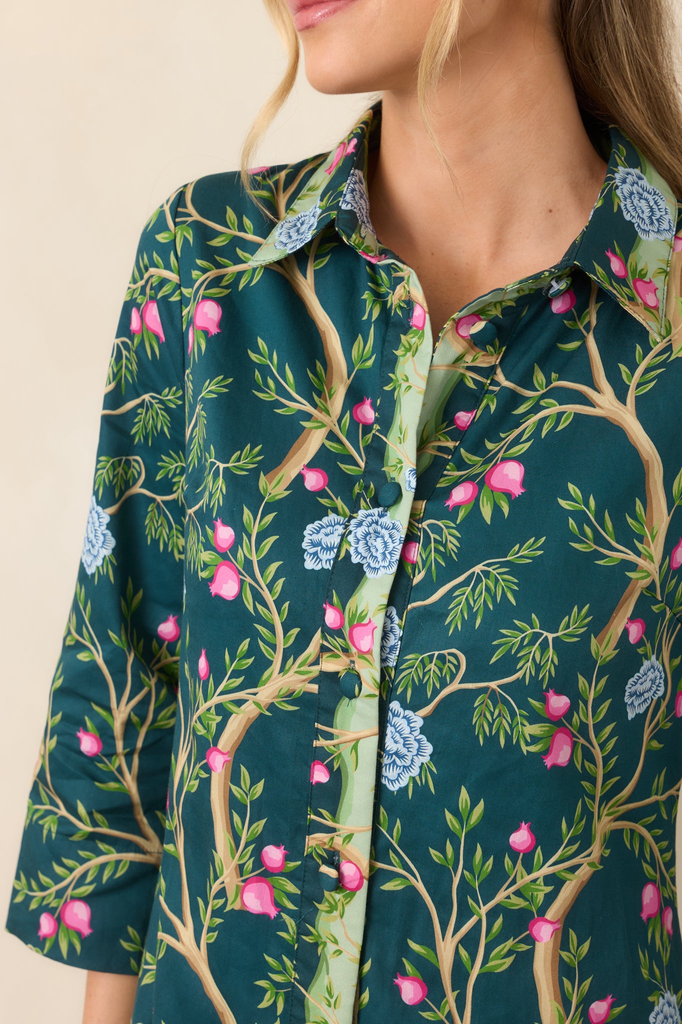Close-up of the teal botanical dress highlighting the contrasting light green floral placket, fabric-covered buttons, and colorful branch-and-flower pattern.