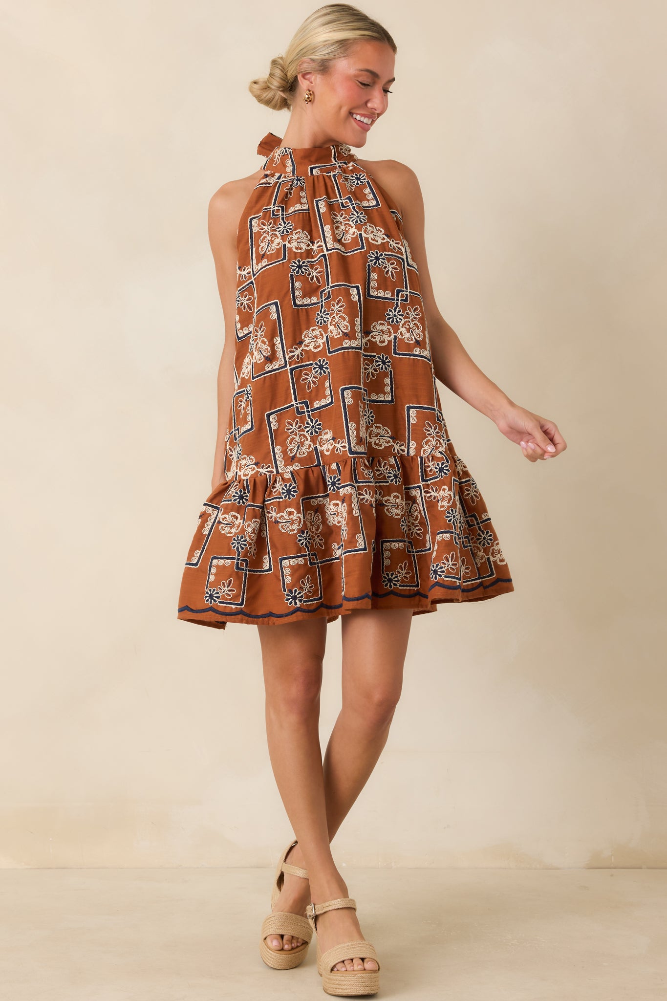 Terracotta embroidered mini dress featuring an ivory and navy pattern, halter neckline, and flounced hem.
