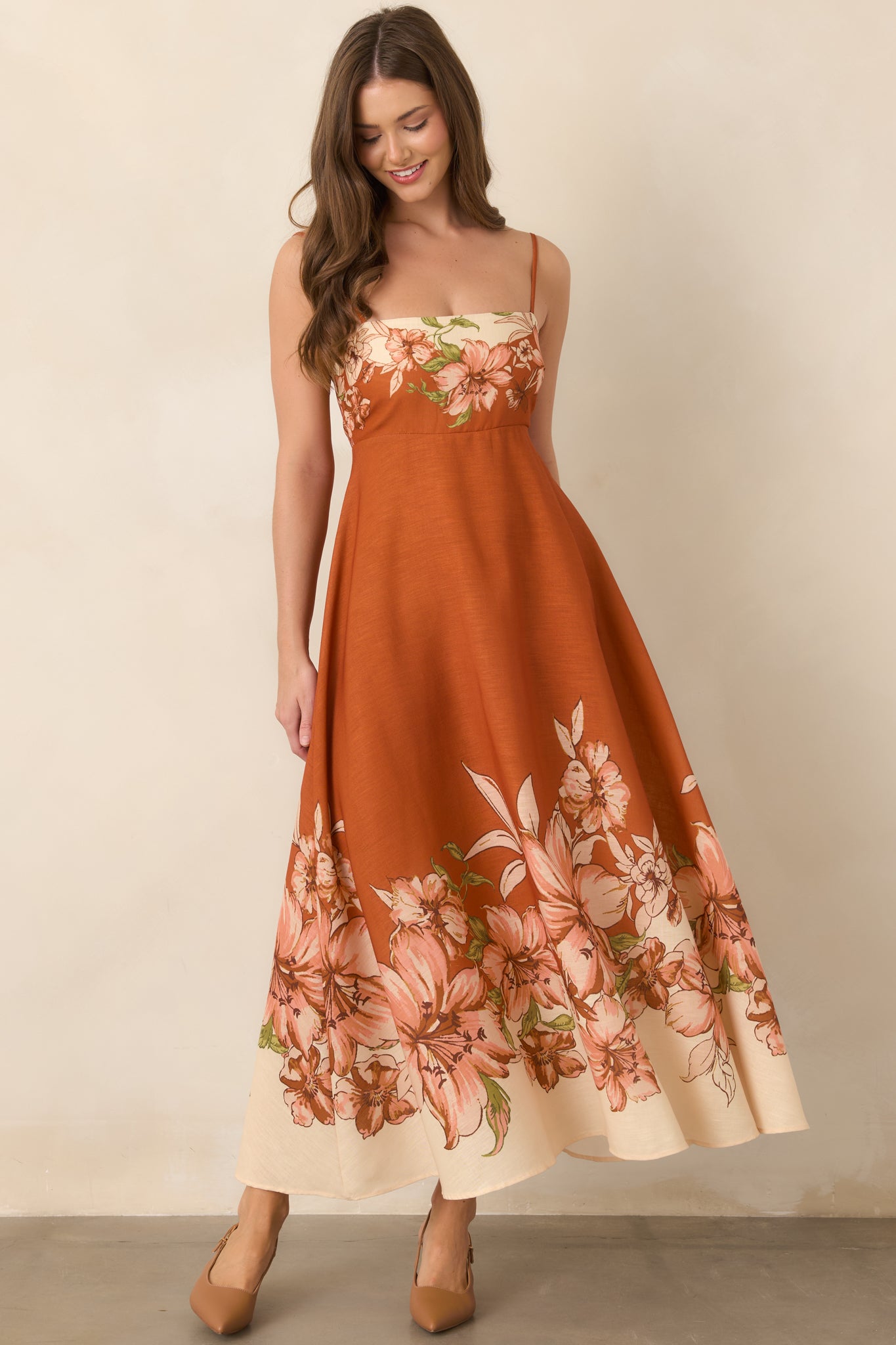 Terracotta floral dress showcasing its fitted upper bodice, delicate straps, bold floral border, and graceful flowing skirt.