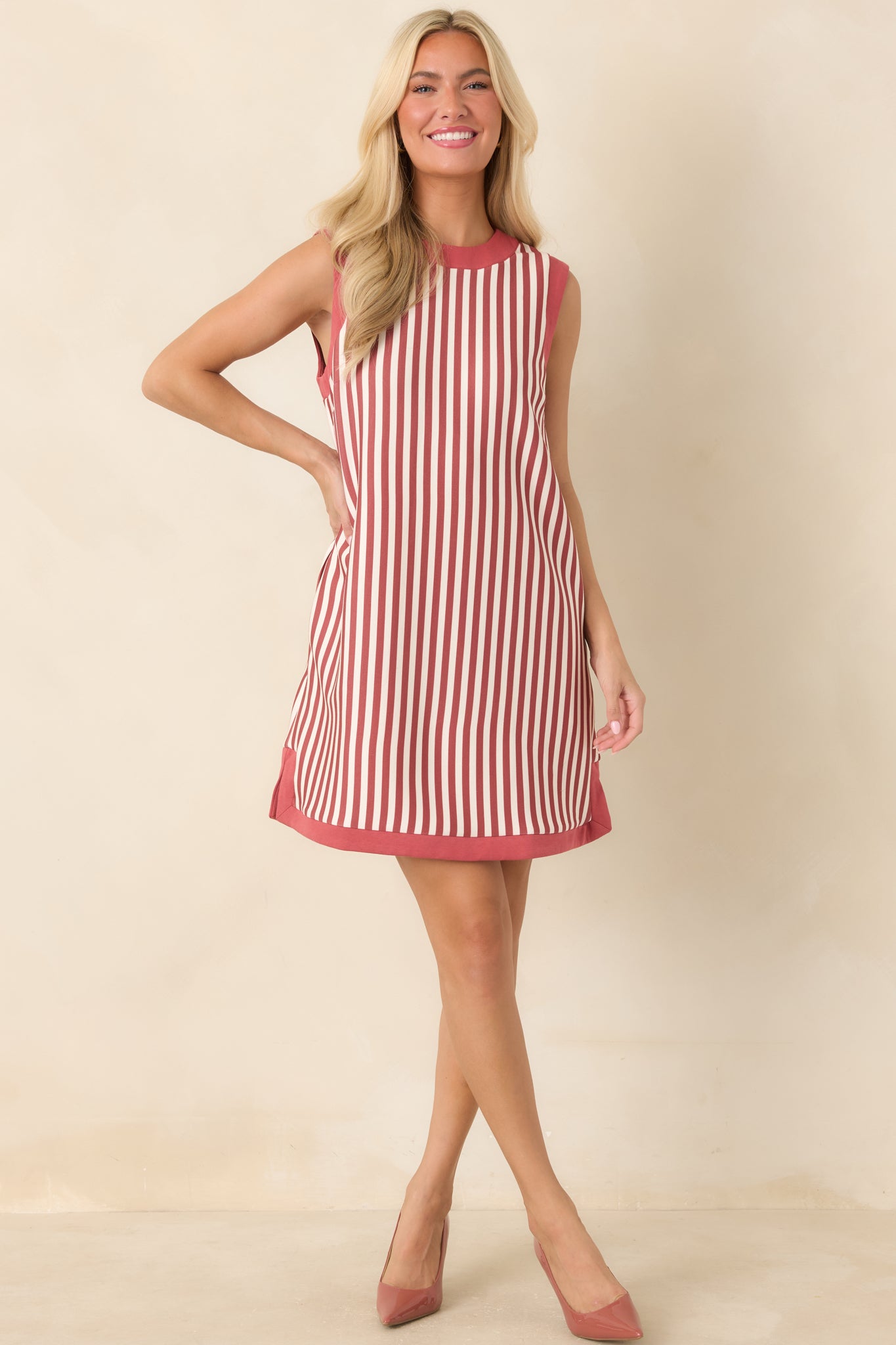 Sleeveless striped mini dress showcasing a relaxed straight shape, alternating terracotta and ivory stripes, and contrasting trim around the neckline and edges.