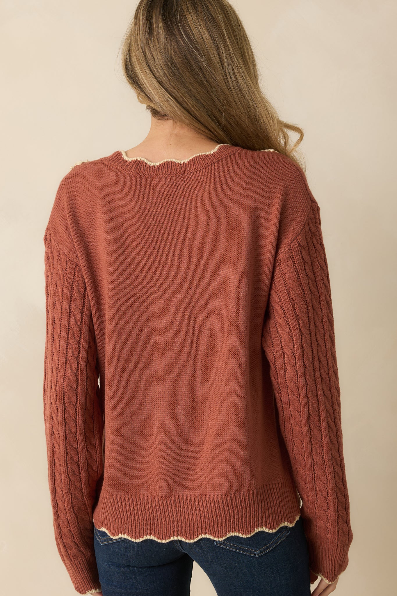 Rear view of the terracotta sweater with a simple cable knit design and long sleeves finished with ribbed cuffs.