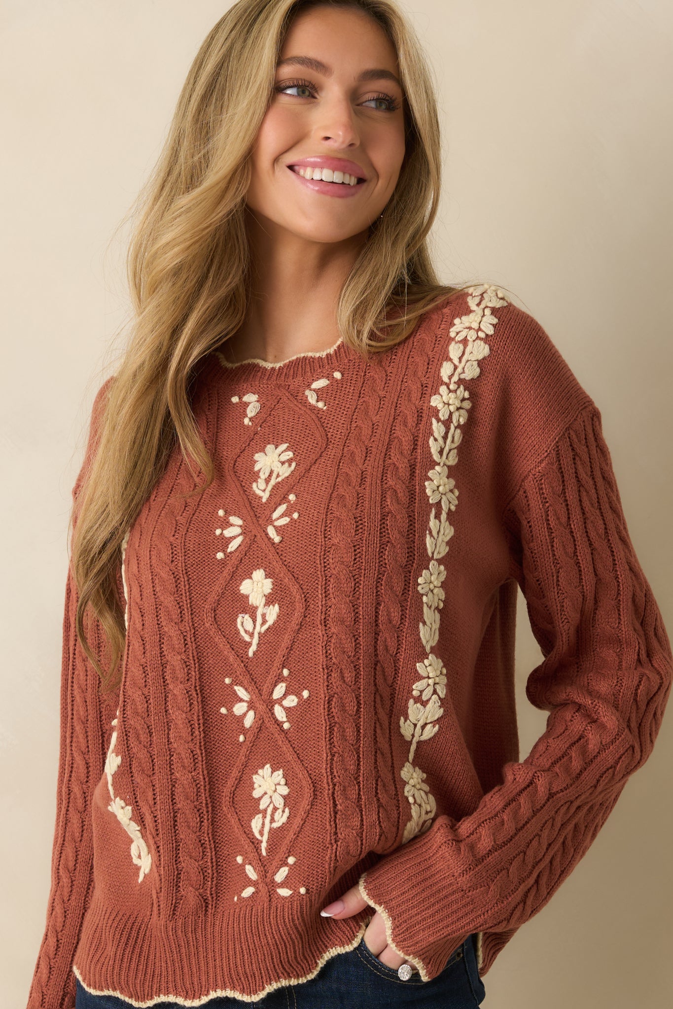 Scalloped edge and ivory floral embroidery shown on the terracotta sweater’s front knit.