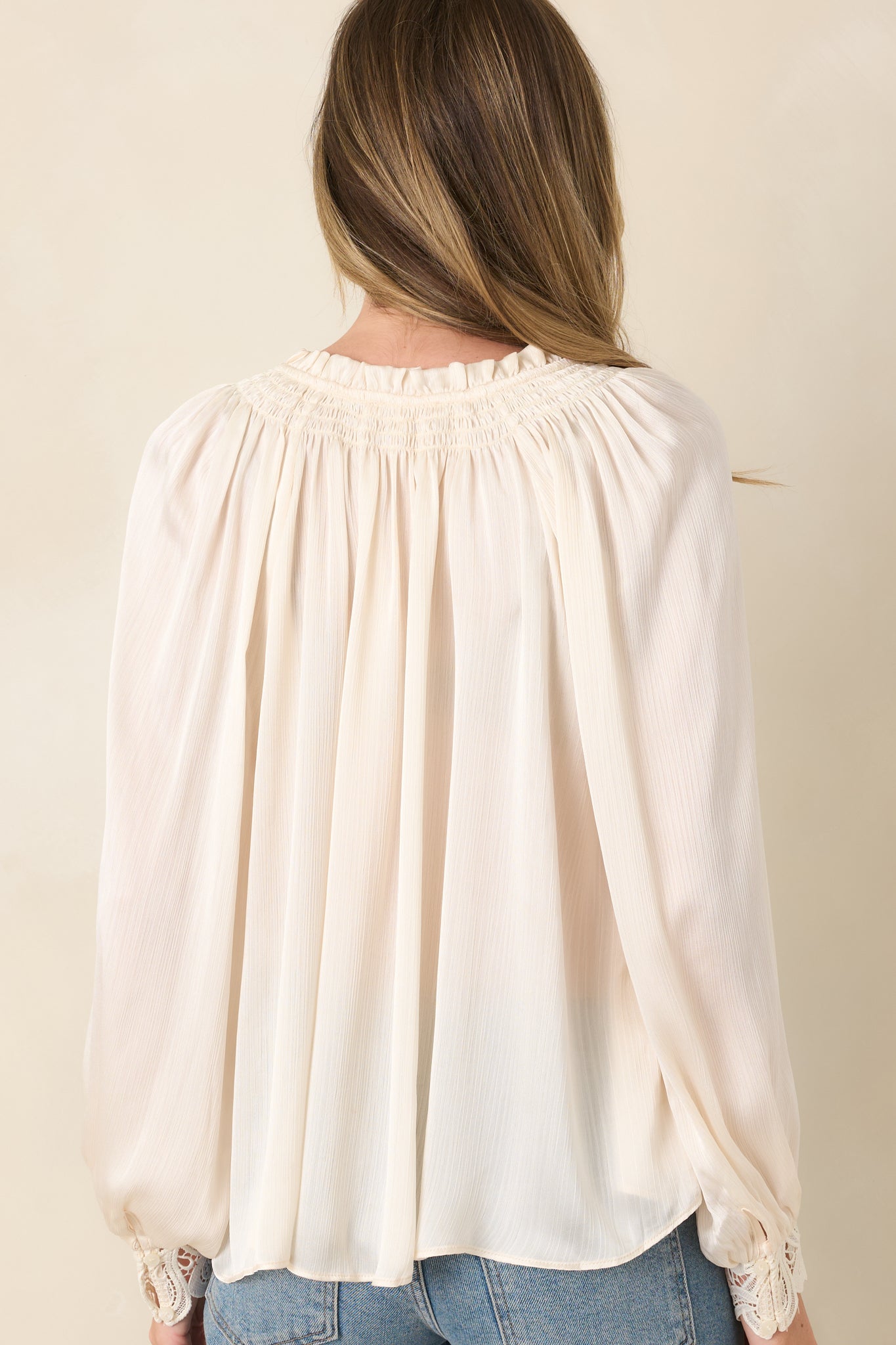 Rear view of the lightly textured blouse featuring a softly gathered back, long balloon sleeves, and intricate lace cuffs.