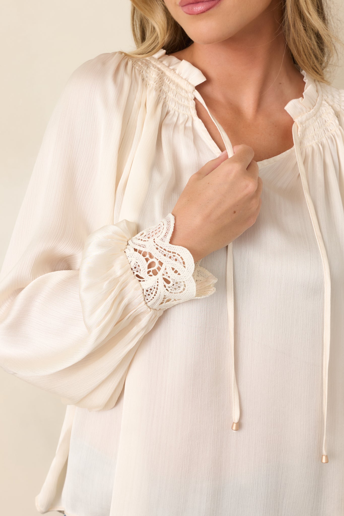 Close-up of the lightly textured fabric highlighting the smocked ruffle neckline, gold-tone tipped ties, lace cuffs, and fine stitching.